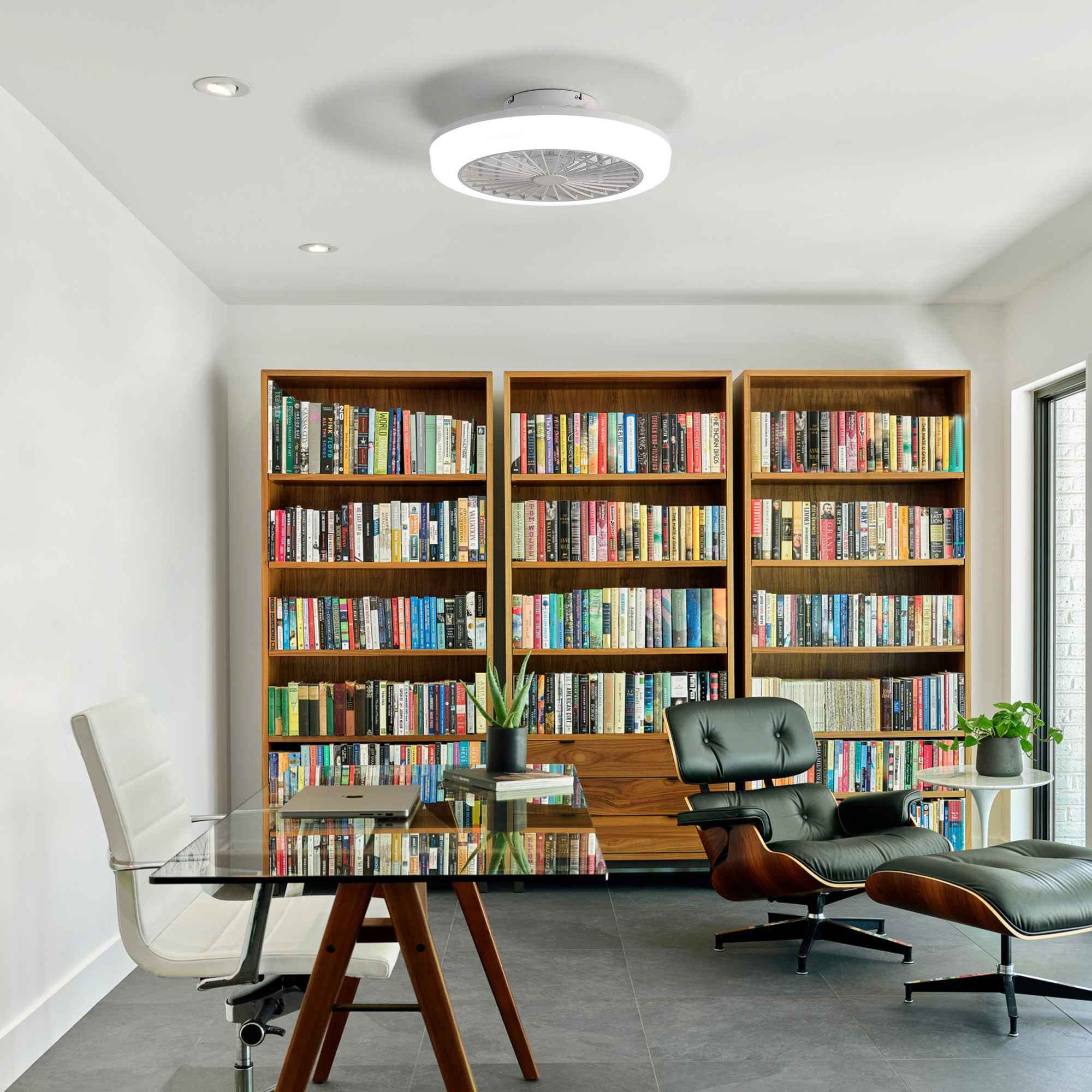 Ein modernes Büro mit Bücherregalen, Glastisch, Ledersessel und Deckenventilator mit Licht.