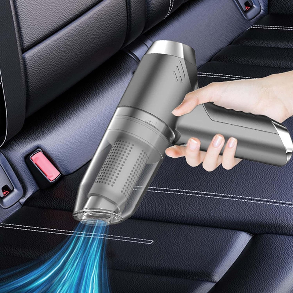 Eine Hand hält einen grauen Handstaubsauger über einem Autositz. Blaue Linien zeigen die Saugwirkung. Der Sitz ist aus schwarzem Leder.