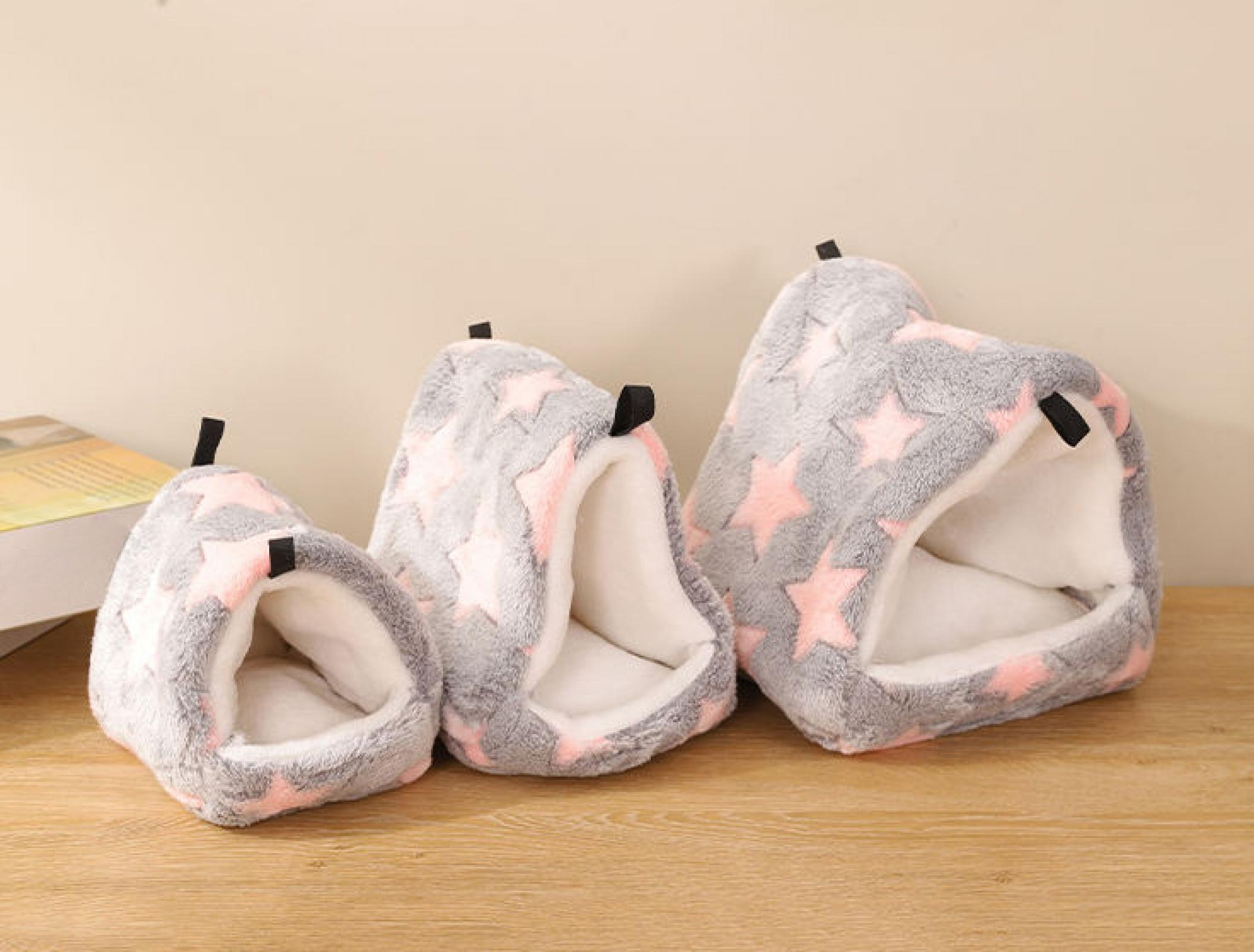 Drei Plüsch-Haustierbetten in verschiedenen Größen. Grau mit rosa Sternen, weißen Innenräumen und schwarzen Griffen. Sie stehen auf Holz.