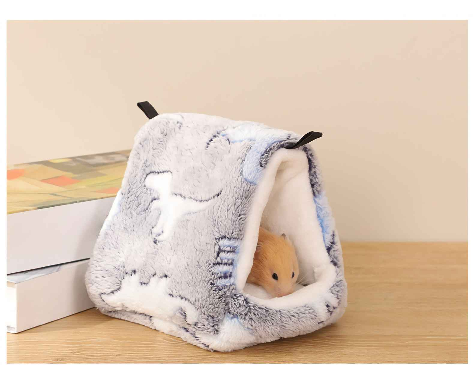Ein Hamster in einem gemütlichen, gemusterten Haus. Das Haus steht auf einer Holzoberfläche. Heller Hintergrund.