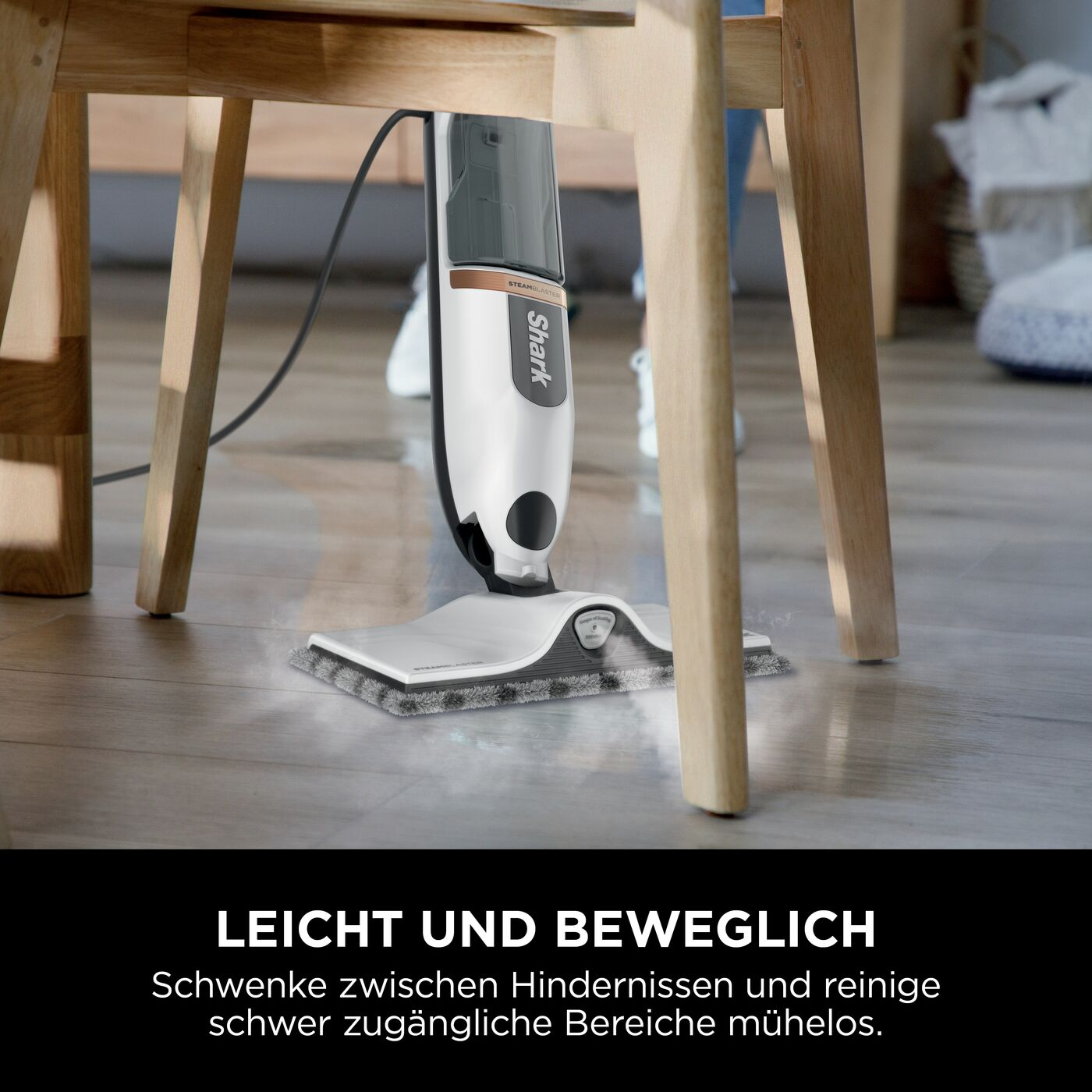 Ein weißer und schwarzer Shark-Dampfmopp reinigt einen Holzboden unter einem Holzstuhl. Dampf ist sichtbar.