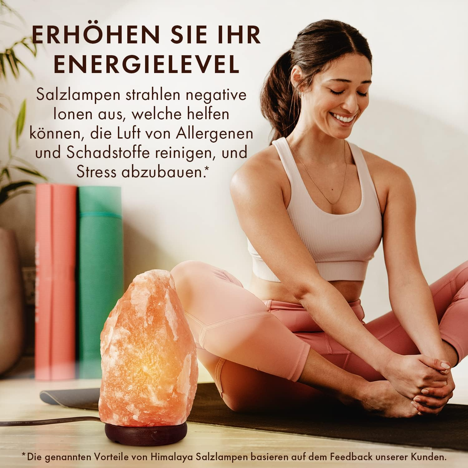 Frau in Trainingskleidung lächelt neben einer beleuchteten Salzlampe. Yogamatten sind im Hintergrund.