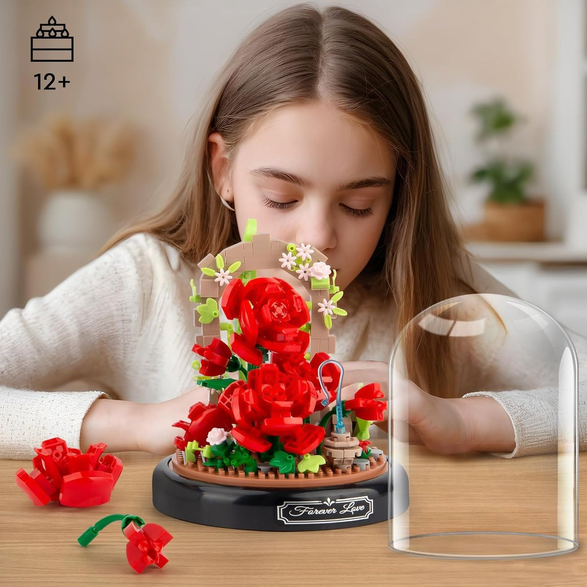 Ein Mädchen betrachtet ein Lego-Rosen-Set. Das Set enthält rote Rosen in einer Glaskuppel, mit losen Teilen. Die Szene ist drinnen.
