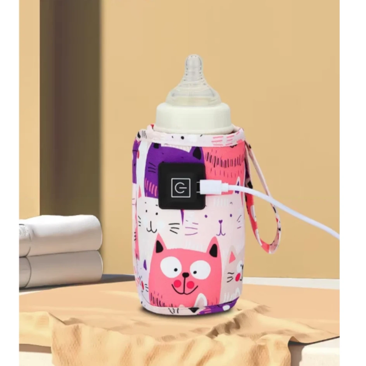 Eine Babyflasche in einem bunten, mit Katzenmotiven versehenen Wärmer. Ein USB-Kabel ist angeschlossen. Der Hintergrund ist beige.