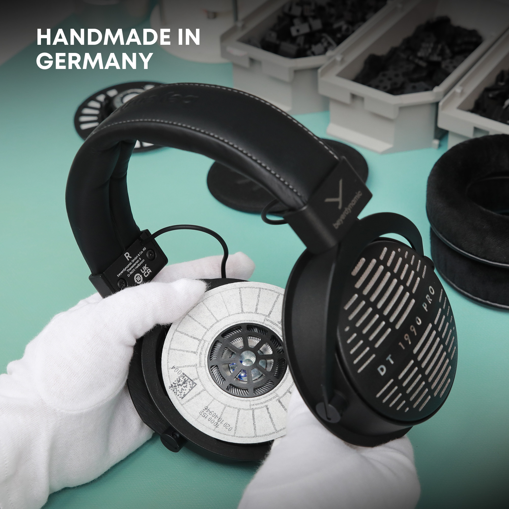Schwarzer Kopfhörer DT 1990 PRO wird zusammengebaut. Text Handmade in Germany. Weiß behandschuhte Hände halten die Teile.