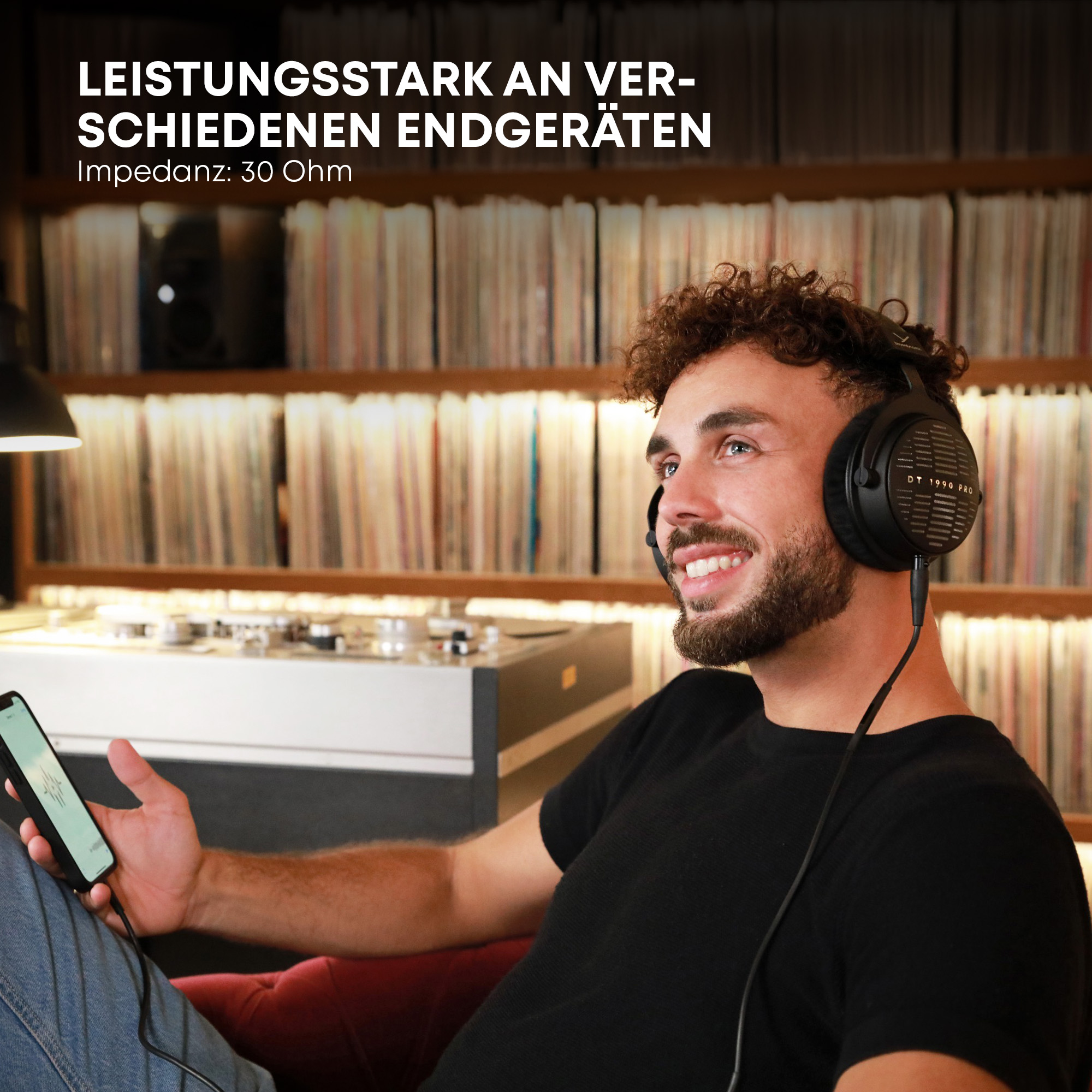 Mężczyzna w słuchawkach i z telefonem. Tło: płyty i gramofon. Uśmiecha się.