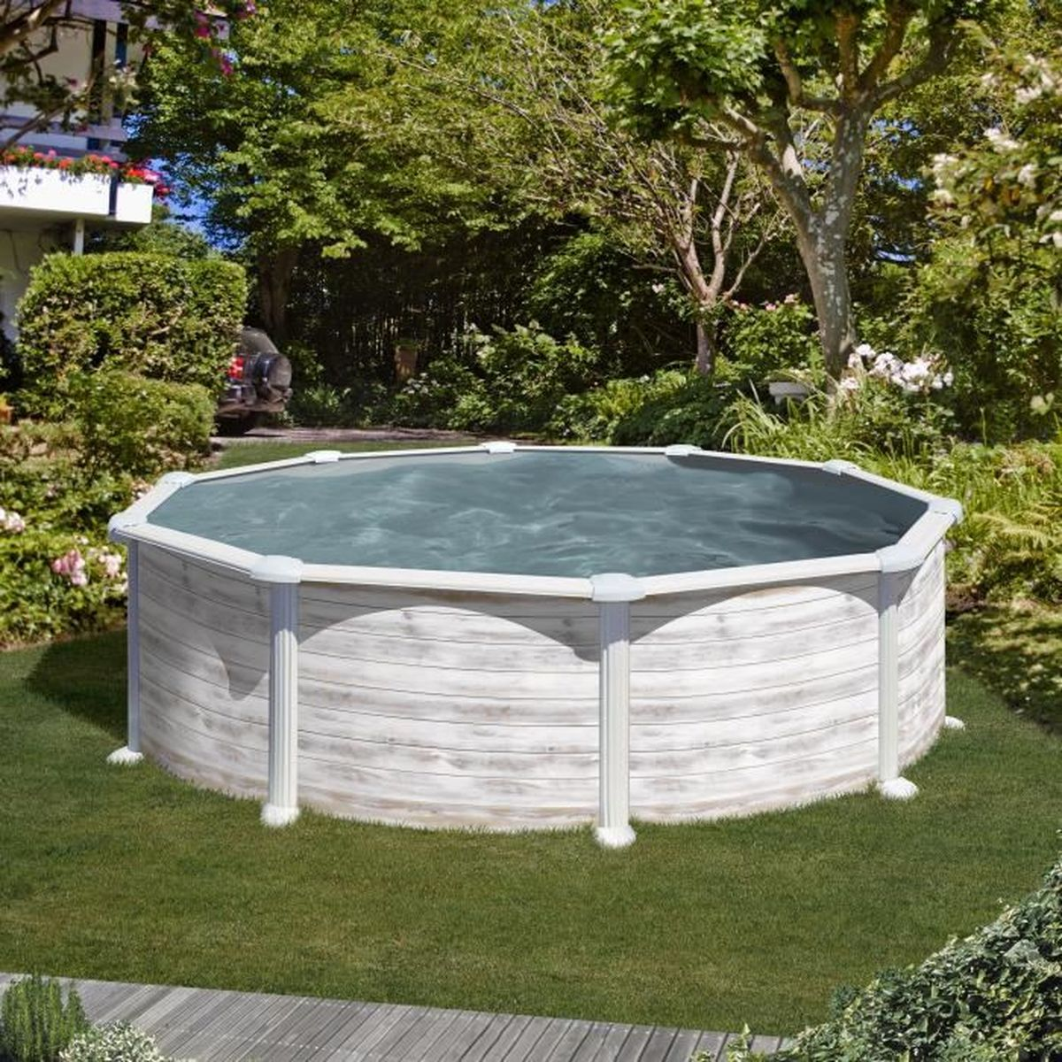 Una piscina elevada se encuentra sobre césped, rodeada de árboles y plantas. La piscina tiene un exterior de madera y está llena de agua.
