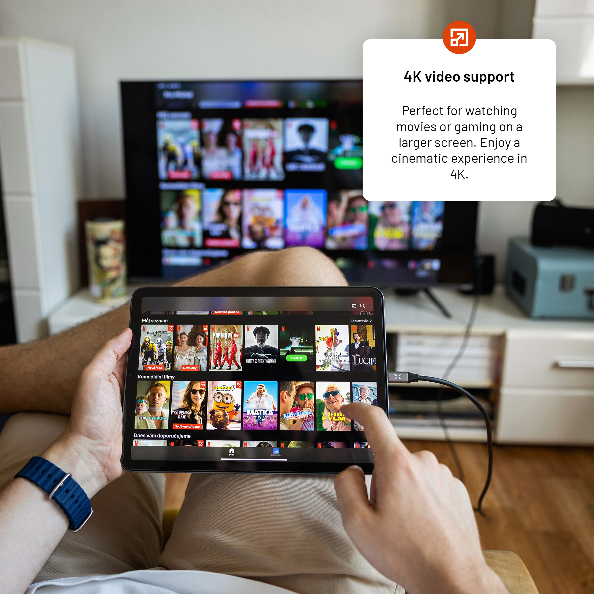 Eine Person hält ein Tablet mit einer Film-Streaming-App, die mit einem Fernseher verbunden ist. Die Szene ist in Innenräumen.
