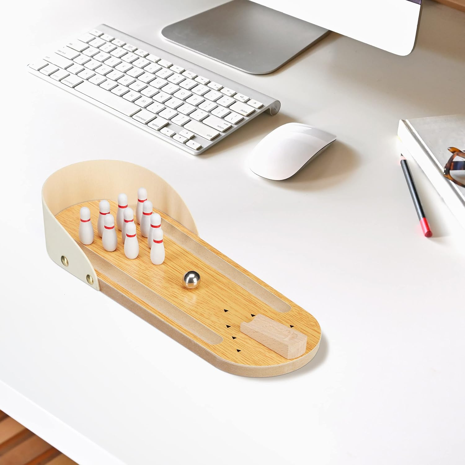 Ein Schreibtisch mit einem Miniatur-Bowling-Spiel, Tastatur, Maus und Monitor. Weiß- und Holztöne dominieren die Szene.