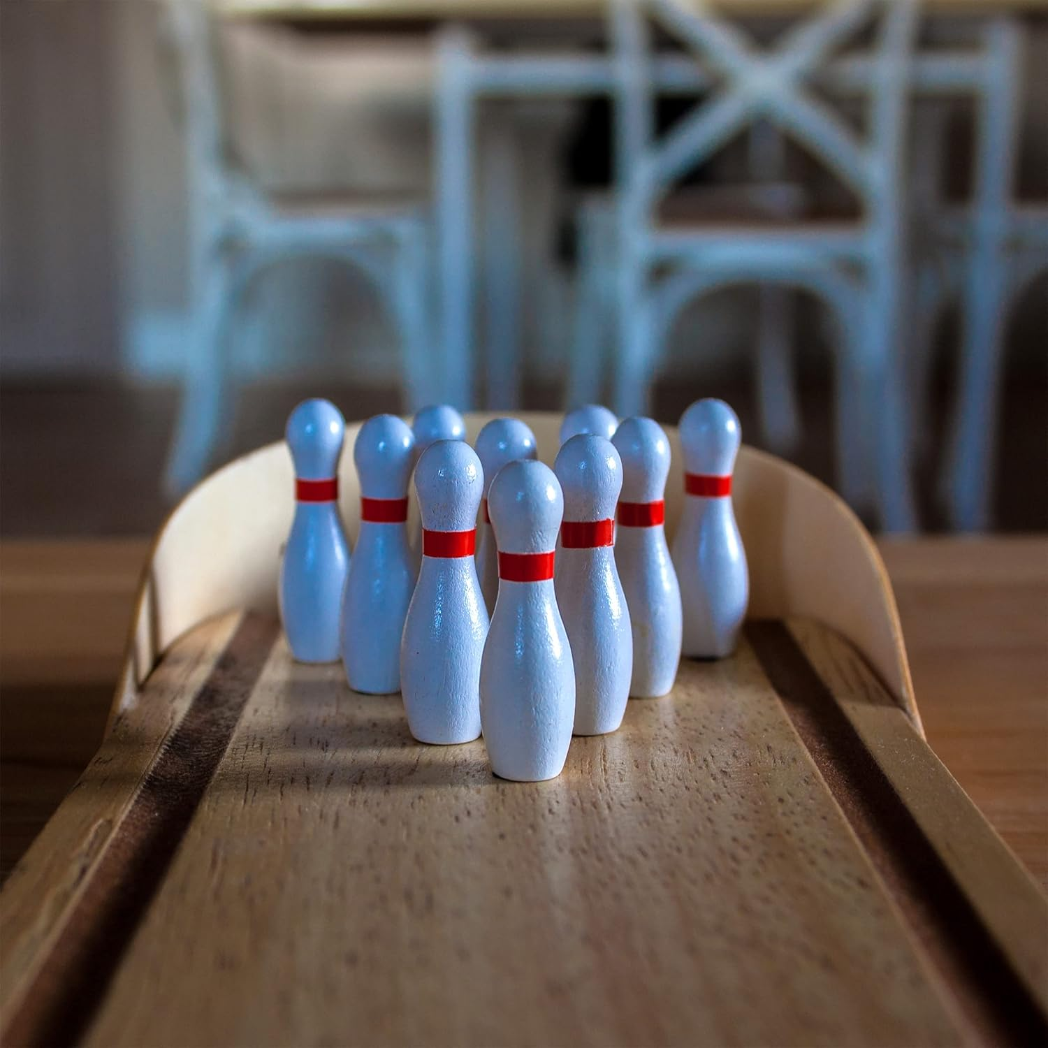 Bowlingkegel mit roten Streifen auf einer Holzspur. Der Hintergrund zeigt einen verschwommenen Raum mit Stühlen.