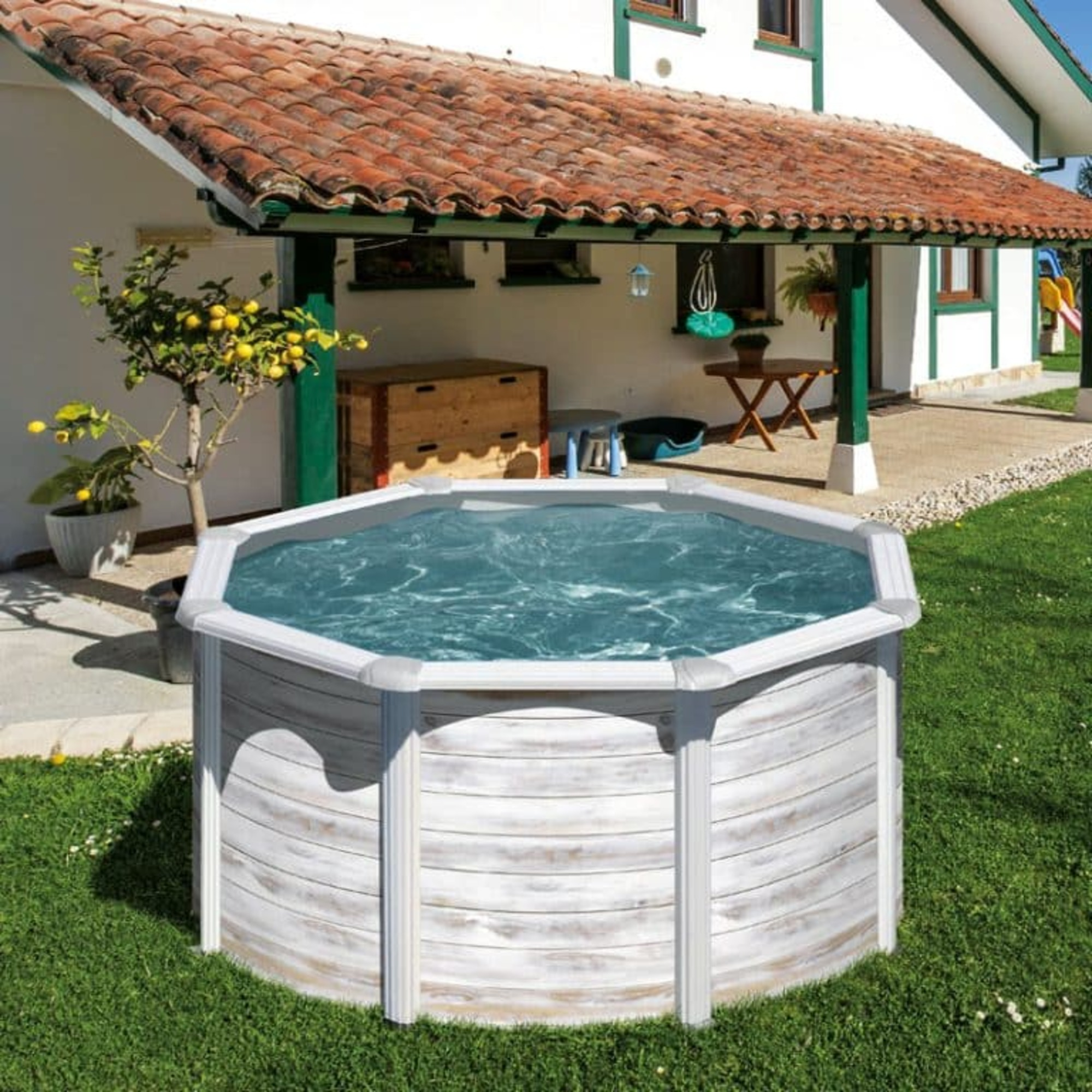 Una piscina elevada se encuentra en un patio con una casa al fondo. A la izquierda hay un árbol con limones.