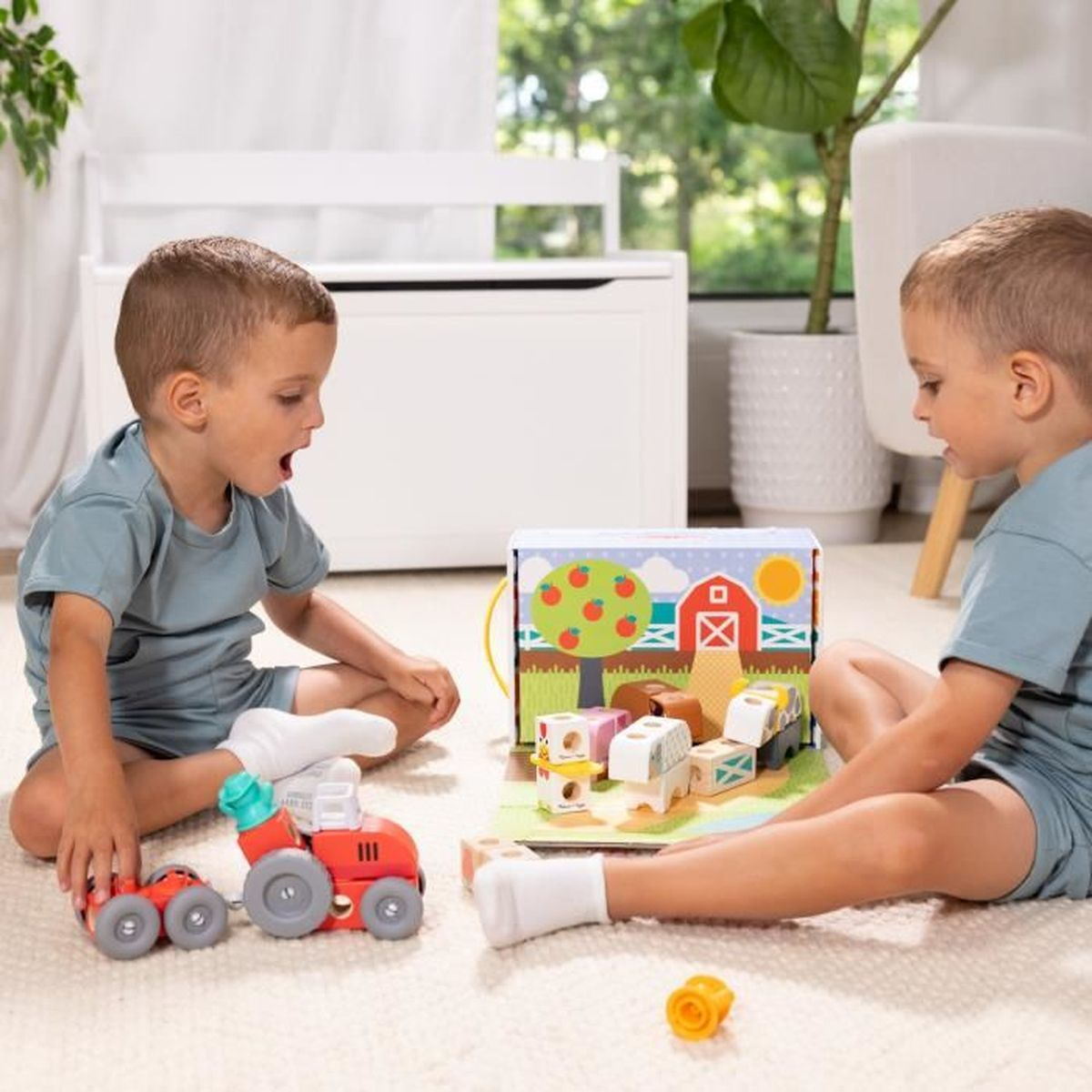 Dos niños juegan con un juego de granja de juguete. Uno mira un tractor rojo, el otro mira la caja de la granja.