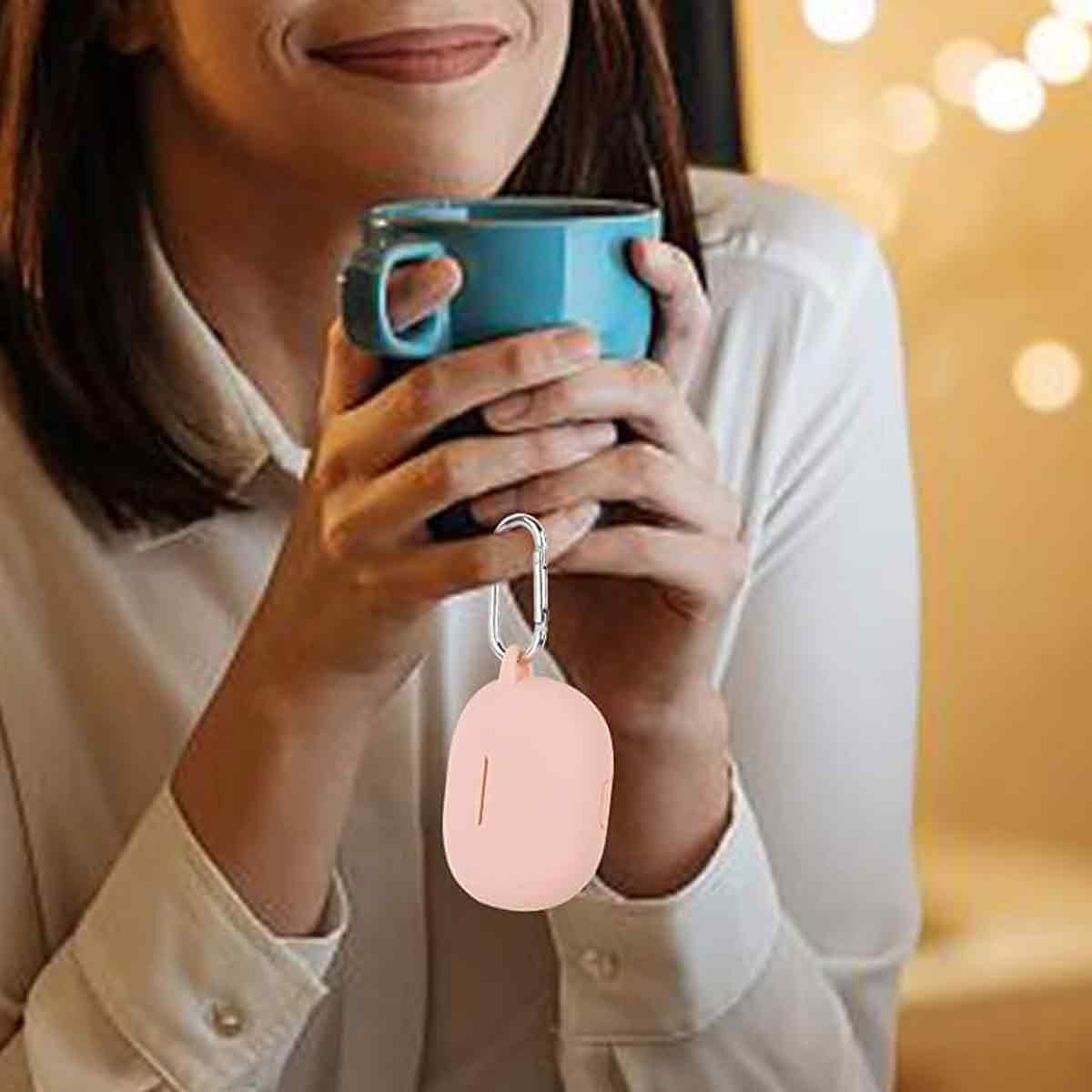 Frau hält einen blauen Becher, darunter hängt ein rosa Kopfhörer-Etui. Bokeh-Hintergrund.