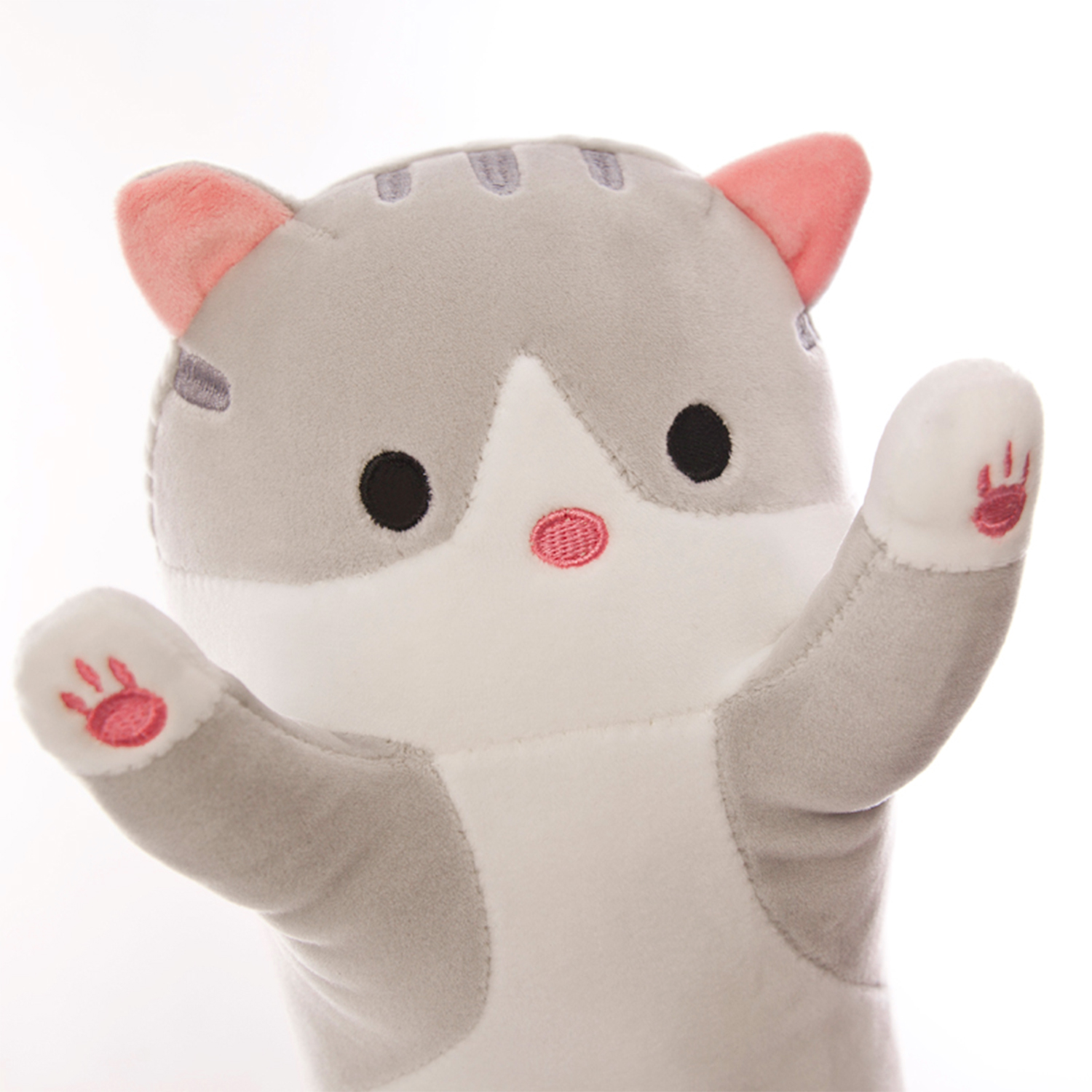 Un peluche a forma di gatto grigio e bianco con orecchie, naso e cuscinetti rosa alza le braccia. Occhi neri e testa a strisce. Sfondo bianco.