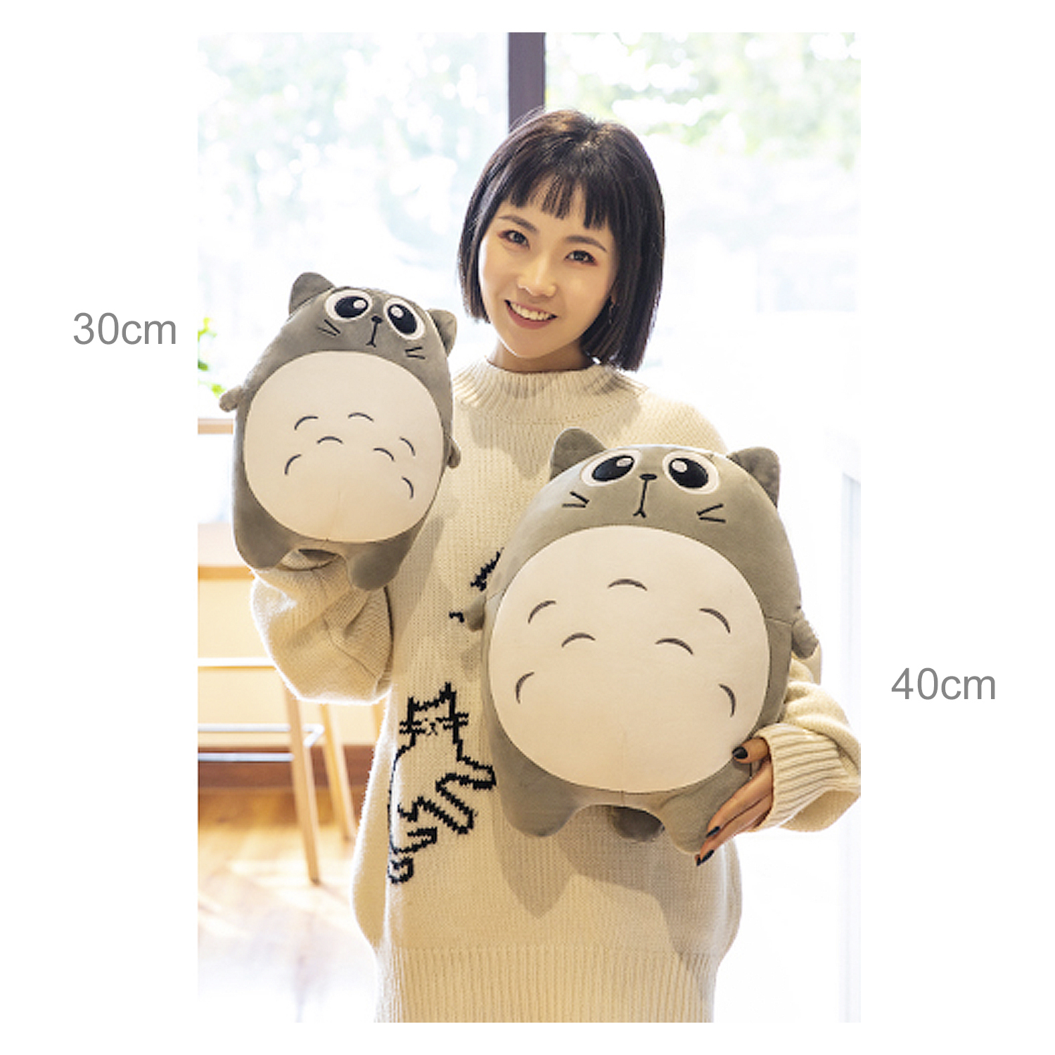 Una donna tiene in mano due peluche di gatto grigio. Indossa un maglione color crema. Le misure di 30 cm e 40 cm sono indicate.