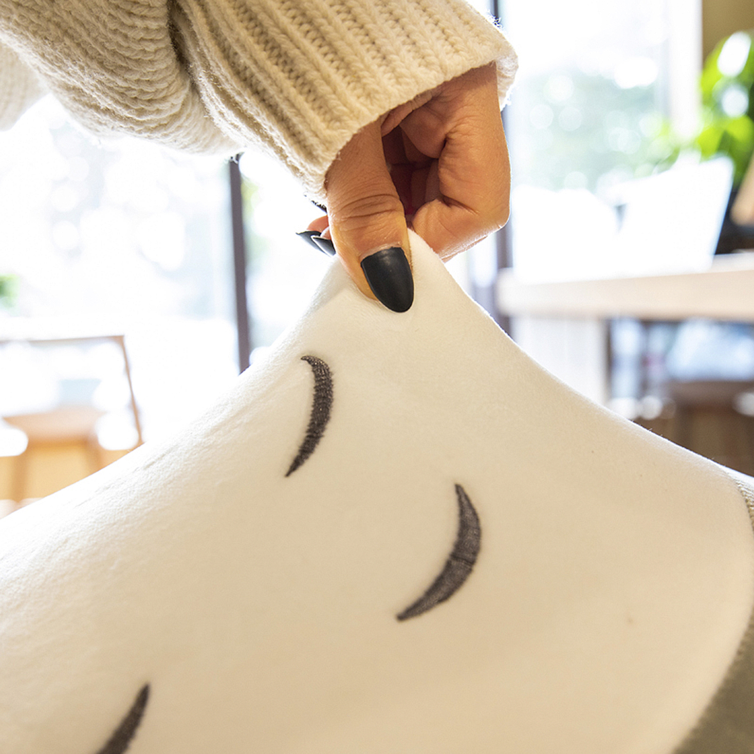 Una mano tiene un cuscino bianco con segni di mezzaluna neri. La mano ha lo smalto nero. Si vede un maglione beige.
