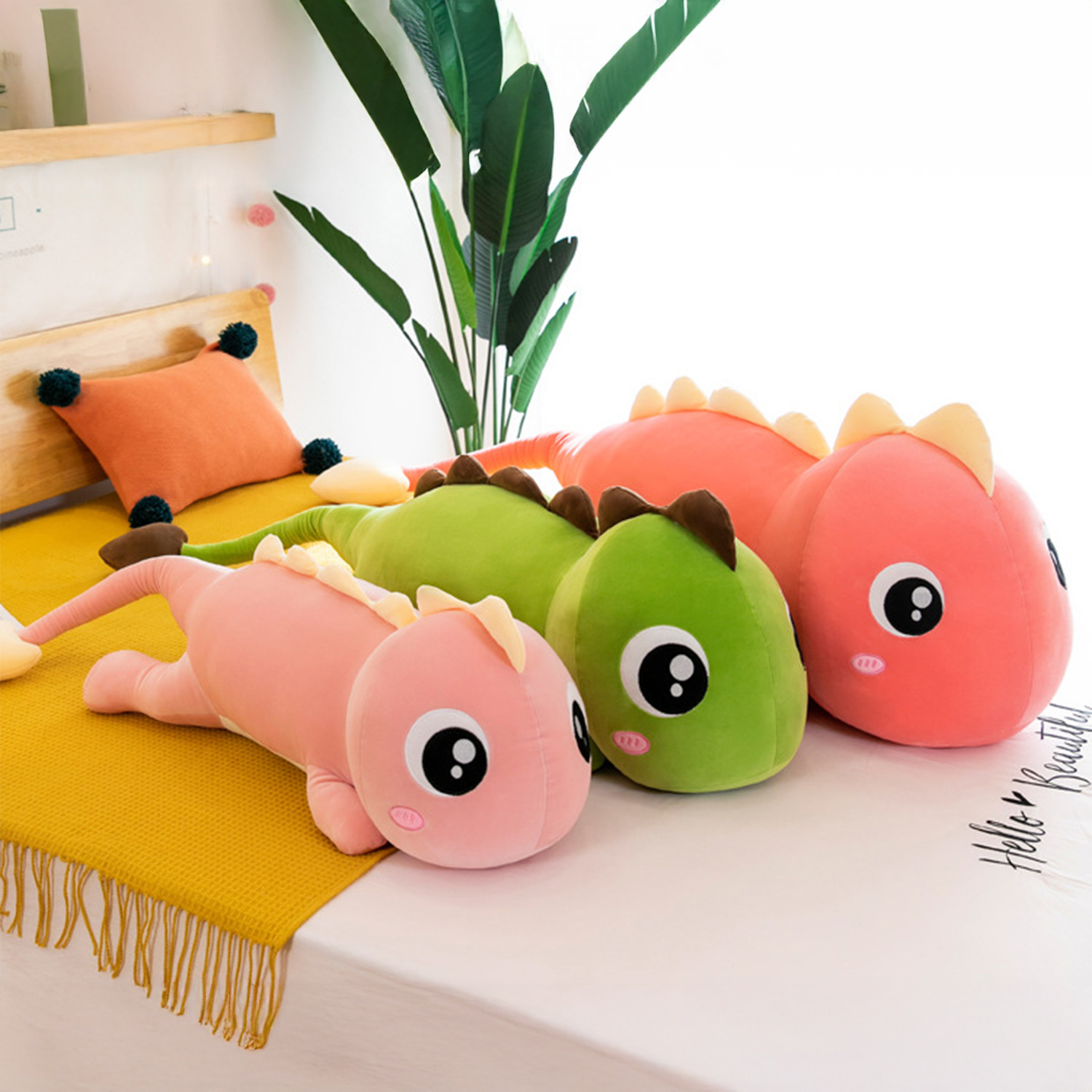 Diversi peluche di dinosauri rosa e verdi su un letto. Sono visibili anche un cuscino arancione e una coperta gialla.