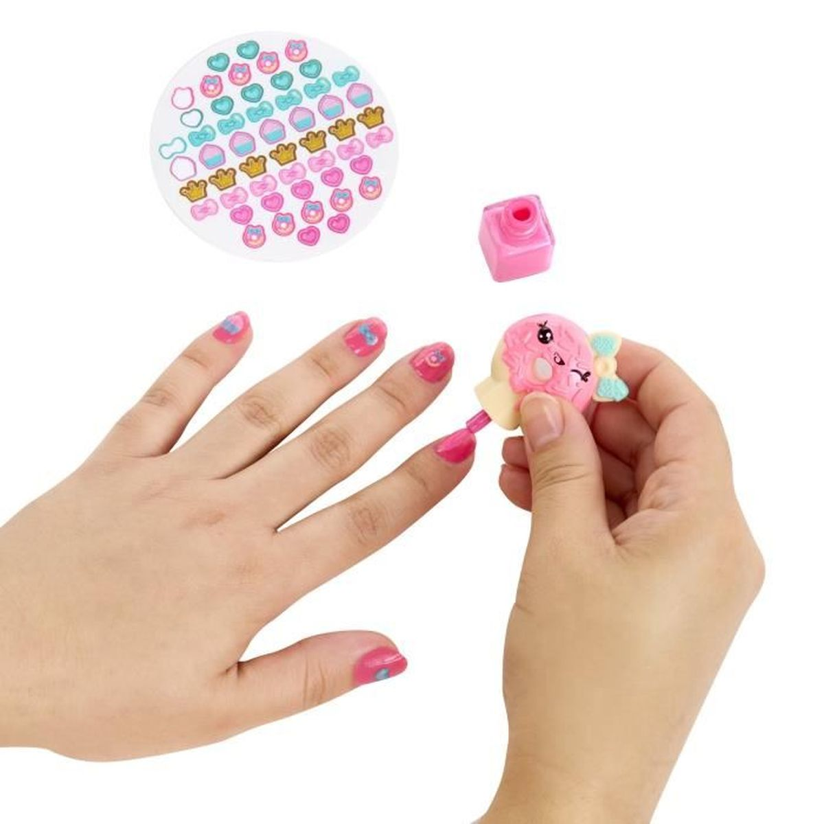 Manos aplicando esmalte de uñas con pegatinas. Uñas rosas, esmalte rosa, pegatinas y un caramelo de juguete. Fondo blanco.