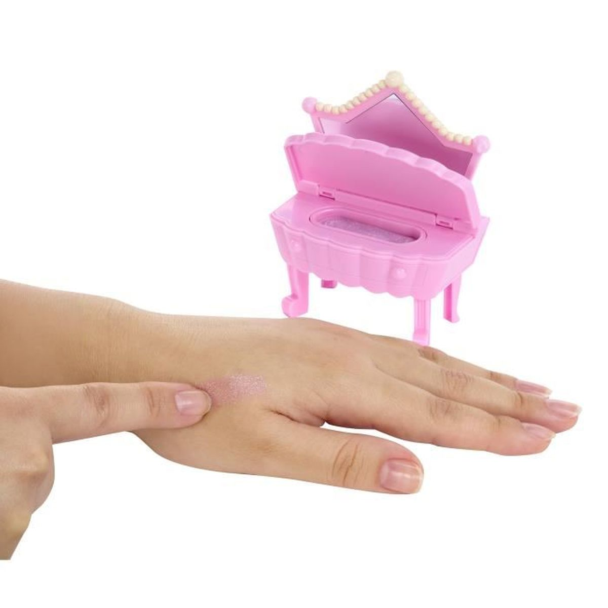 Una mano señala purpurina en el dorso de otra mano. Un tocador de juguete rosa con espejo se encuentra en el fondo.