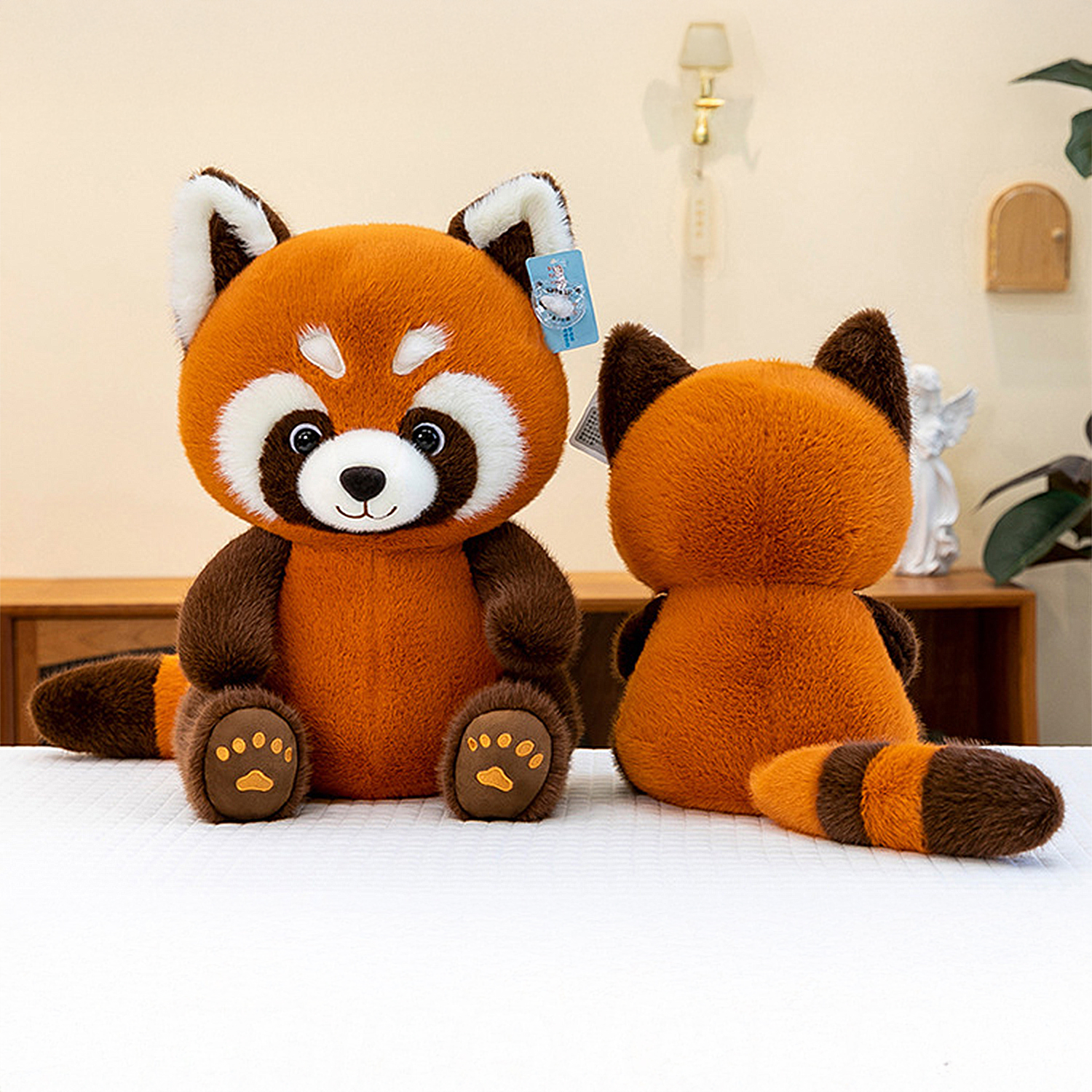 Due panda rossi di peluche. Uno è rivolto in avanti, l'altro di spalle. Entrambi hanno pelliccia arancione, dettagli marroni e sono su una superficie bianca.