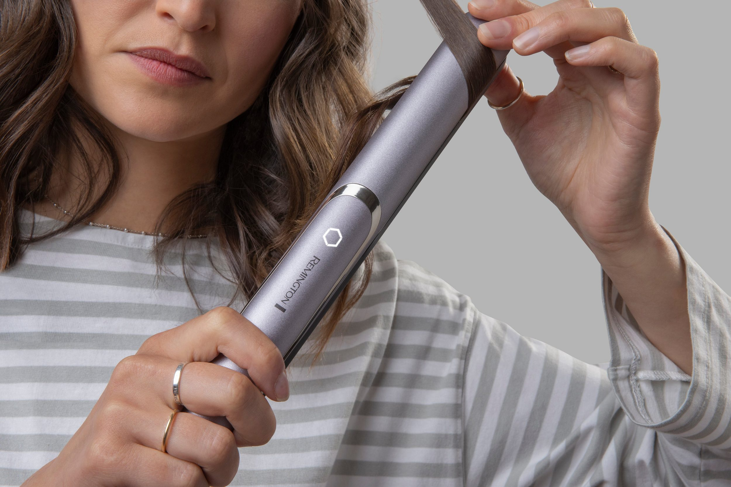 Una donna usa una piastra Remington. Tiene lo strumento vicino al viso, con i capelli tra le piastre.