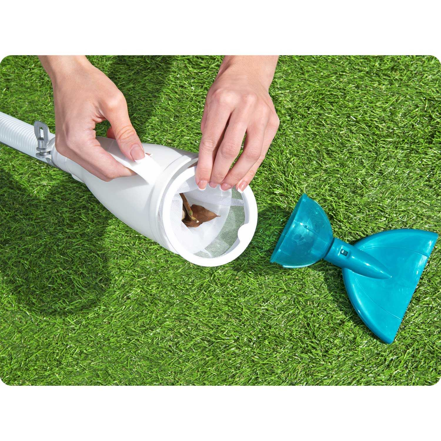 Manos abren un limpiador de piscina blanco para quitar una hoja. Un cabezal limpiador azul está sobre la hierba verde.