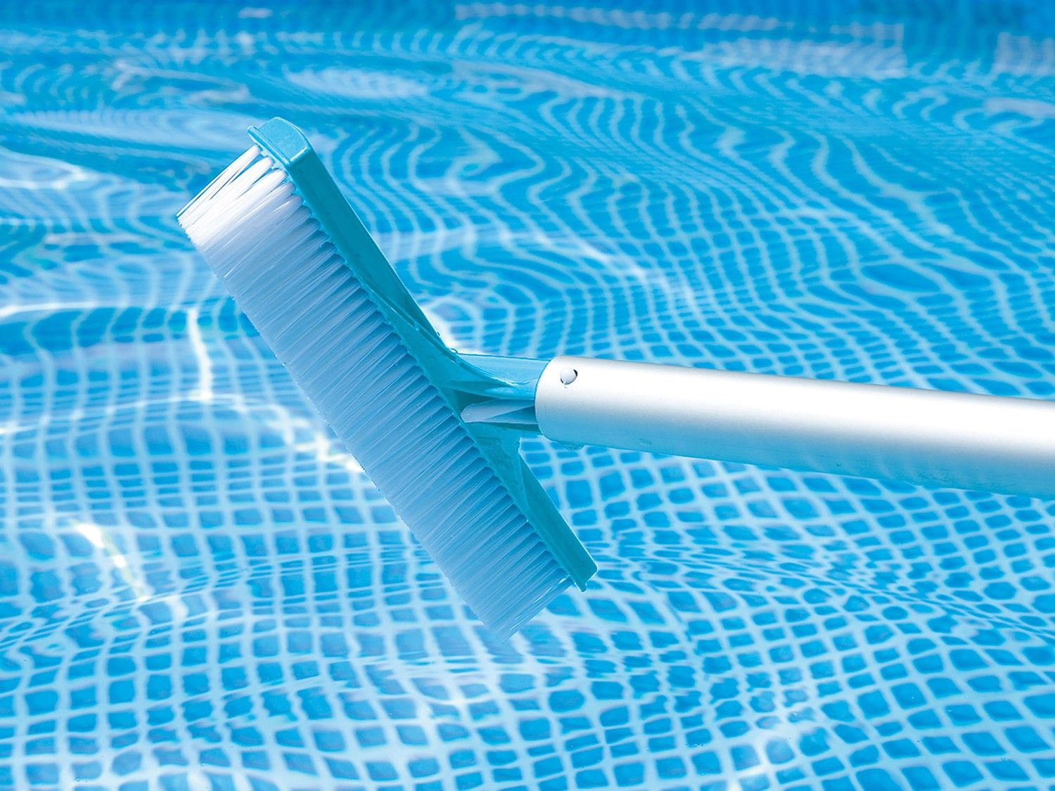 Un cepillo de piscina en una piscina con agua azul. El cepillo es azul claro con cerdas blancas y un mango plateado.