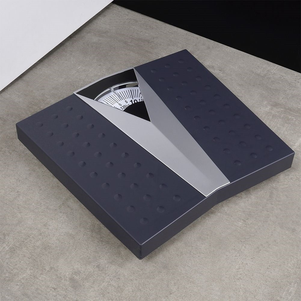 Báscula de baño gris oscuro con centro plateado y dial con medidas de peso, colocada sobre una superficie gris.