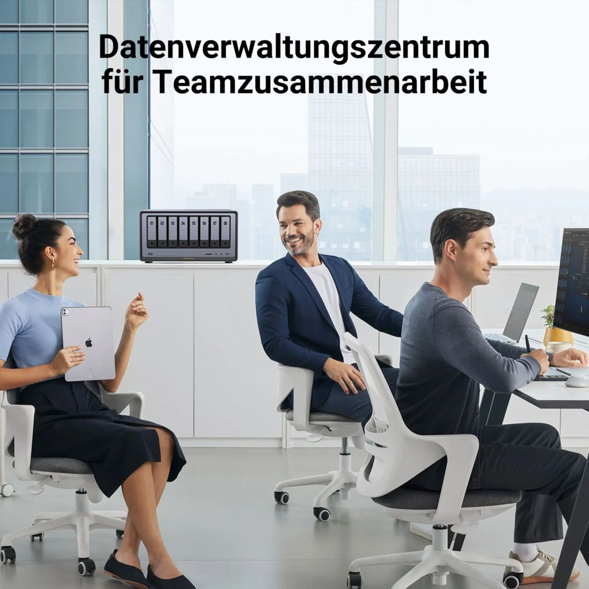 Drei Personen in einem Büro. Eine Frau hält ein Tablet. Zwei Männer sitzen an Computern. Ein Datenspeichergerät steht im Regal.