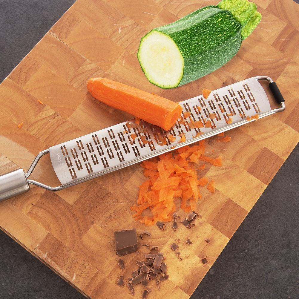 Una zanahoria y un calabacín están en una tabla de cortar de madera con un rallador. También hay zanahorias ralladas y chocolate.
