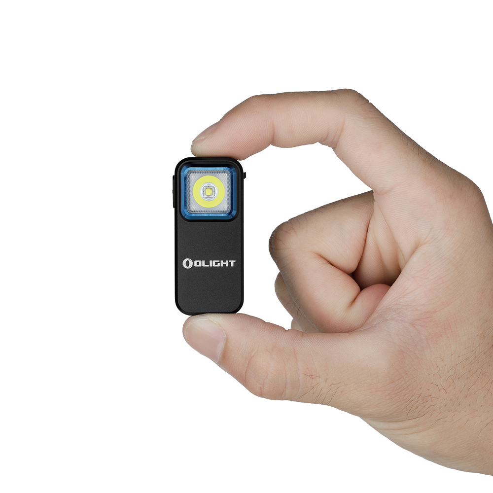 Una mano tiene una piccola torcia nera con una luce bianca brillante. La luce ha un bordo blu e il marchio Olight.
