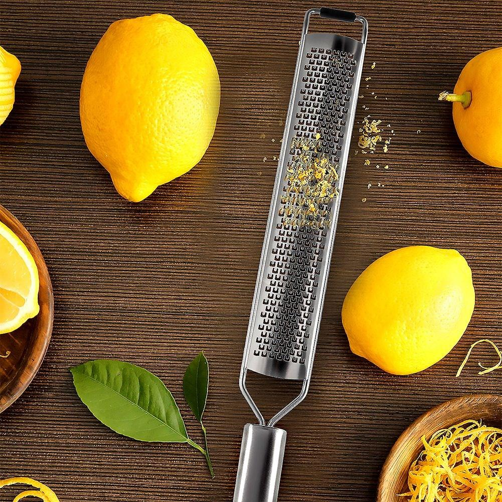 Limones, un rallador y ralladura de limón sobre madera. También hay hojas verdes y cáscara de limón.