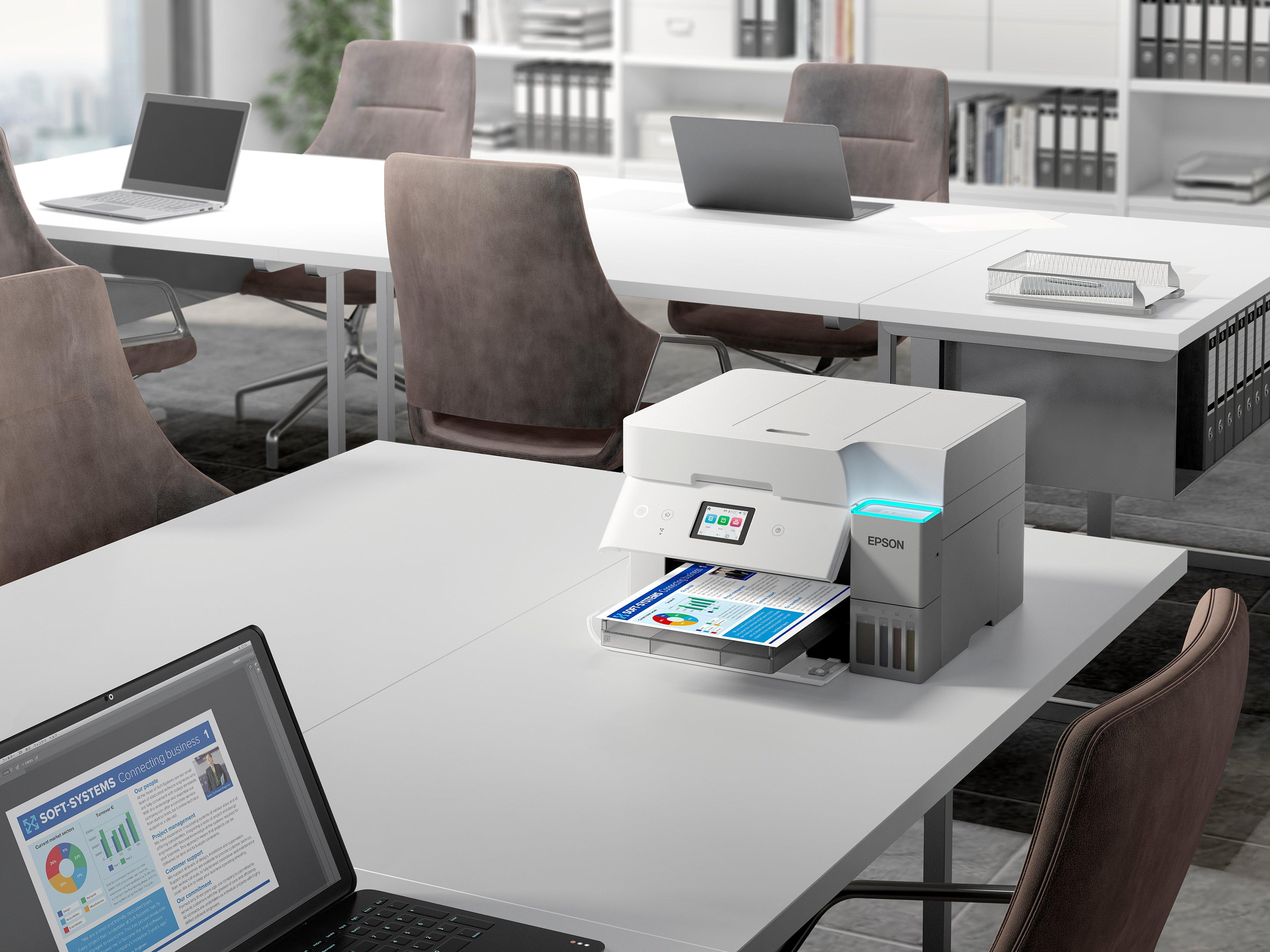 Biuro z białymi biurkami, laptopami, brązowymi krzesłami i drukarką Epson drukującą kolorowy dokument.