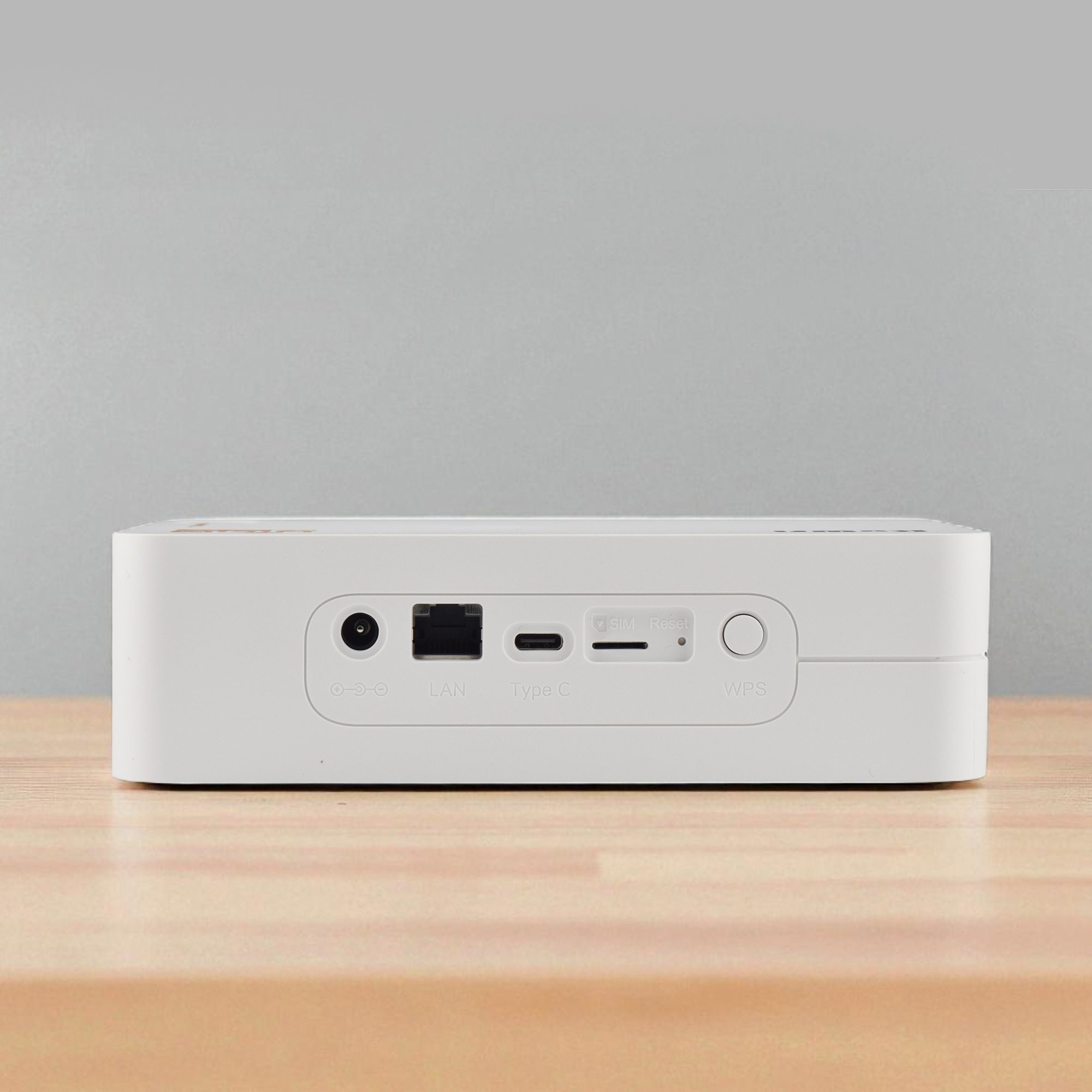 Ein weißer Router steht auf einem Holztisch. Es hat Anschlüsse mit den Bezeichnungen LAN, Typ C, SIM und WPS. Der Hintergrund ist grau.