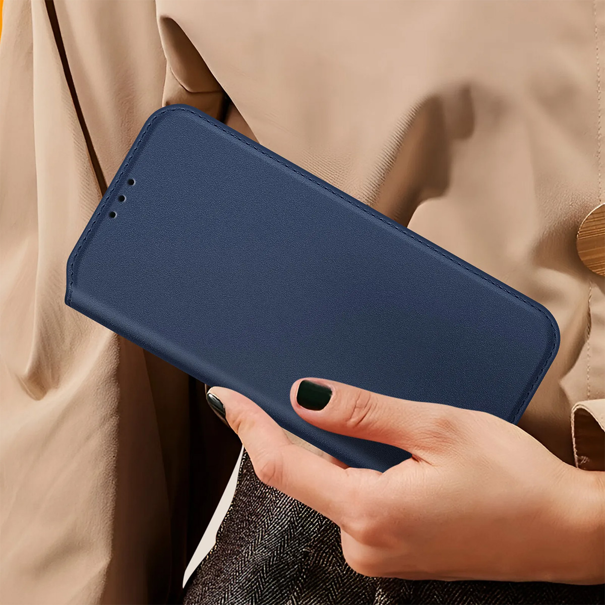 Una mano tiene una custodia blu per telefono. Lo sfondo mostra una giacca beige e una mano con smalto scuro.