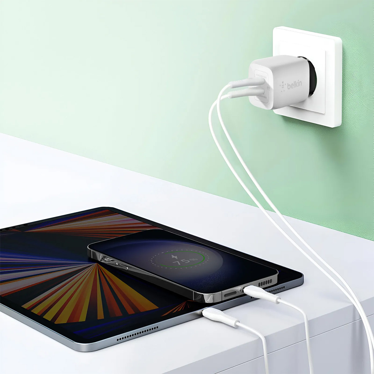 Un caricabatterie Belkin bianco collegato a una presa a muro, che carica un telefono e un tablet. Il telefono mostra il 75% di batteria.
