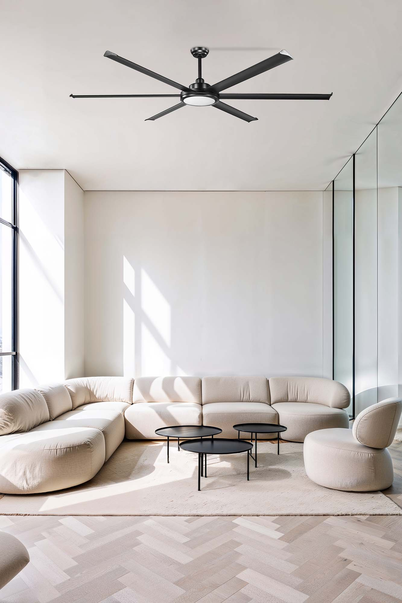 Soggiorno moderno con ventilatore a soffitto nero, divano beige e tavolini neri. Grandi finestre e pavimenti in legno.