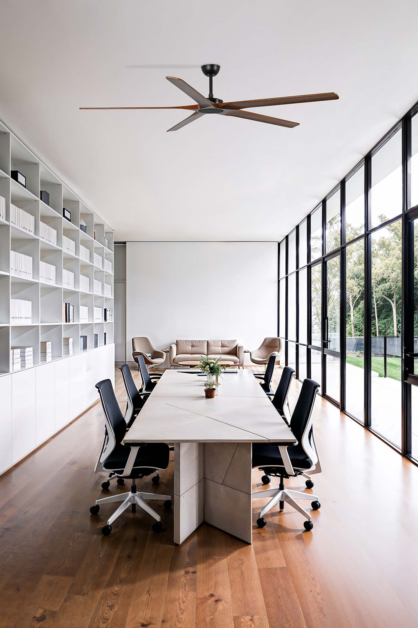 Una moderna sala riunioni con un grande tavolo, sedie nere e un ventilatore a soffitto. Grandi finestre offrono la vista.
