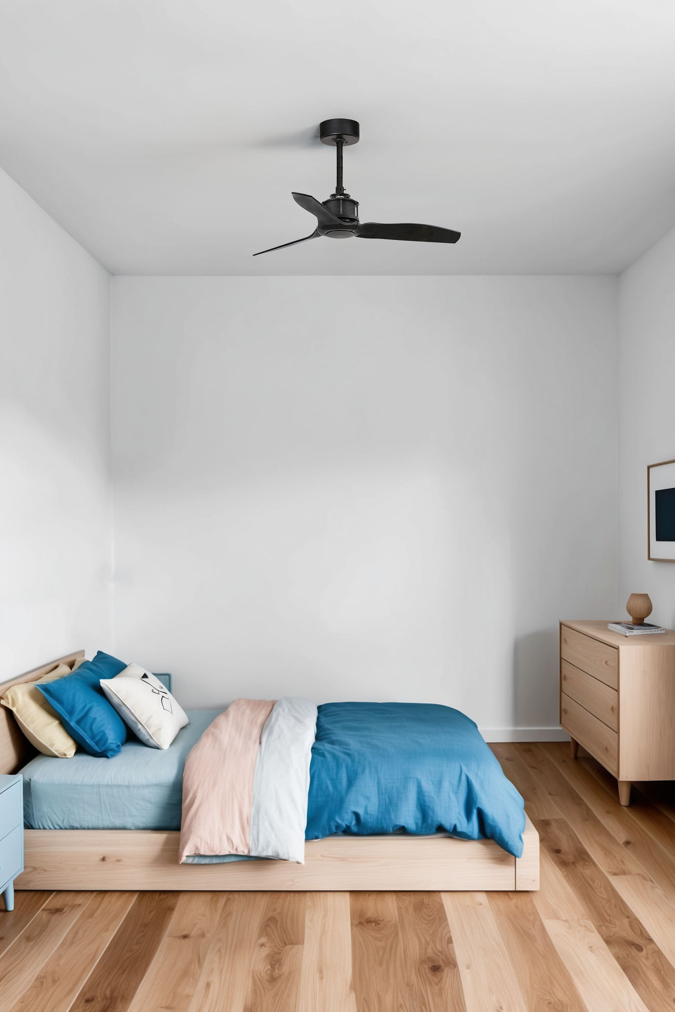 Schlafzimmer mit Holzboden, Bett mit blauer und rosafarbener Bettwäsche und Deckenventilator. Kommode und Bilderrahmen rechts.