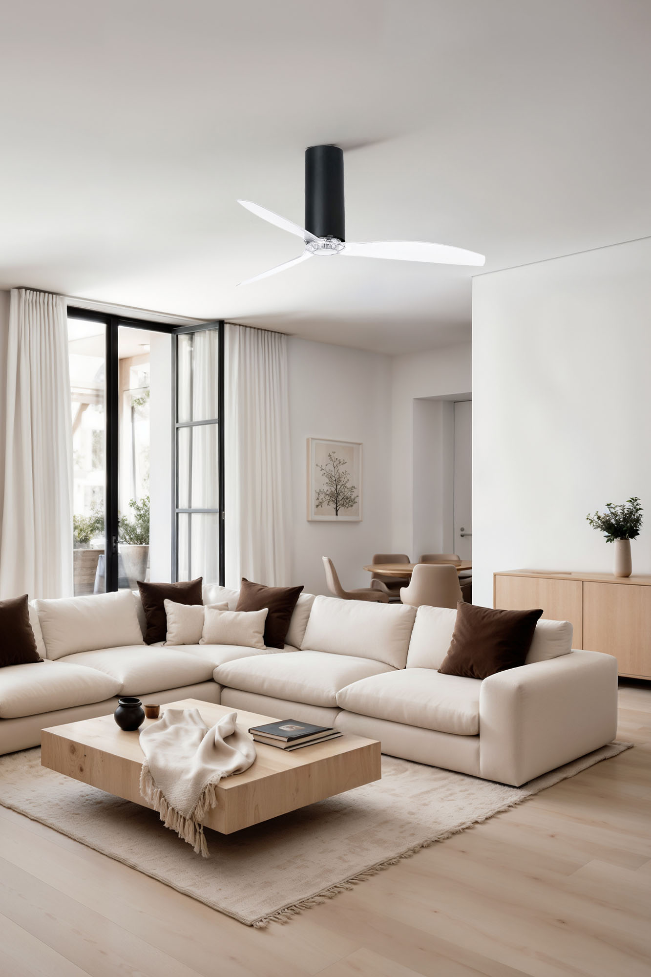 Ein modernes Wohnzimmer mit weißem Ecksofa, Holztisch und Deckenventilator. Große Fenster und helle Farben.