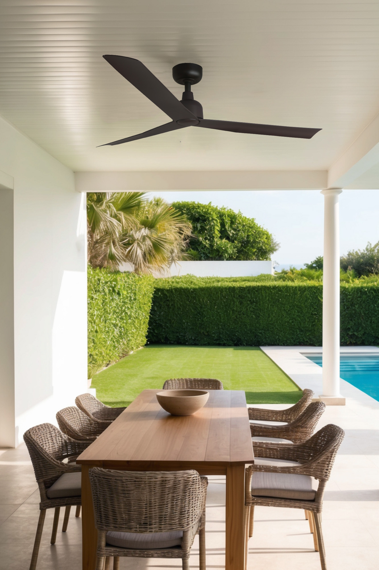 Essbereich im Freien mit Tisch und Stühlen. Ein Deckenventilator hängt darüber. Der Hintergrund zeigt einen Pool und eine grüne Wiese.