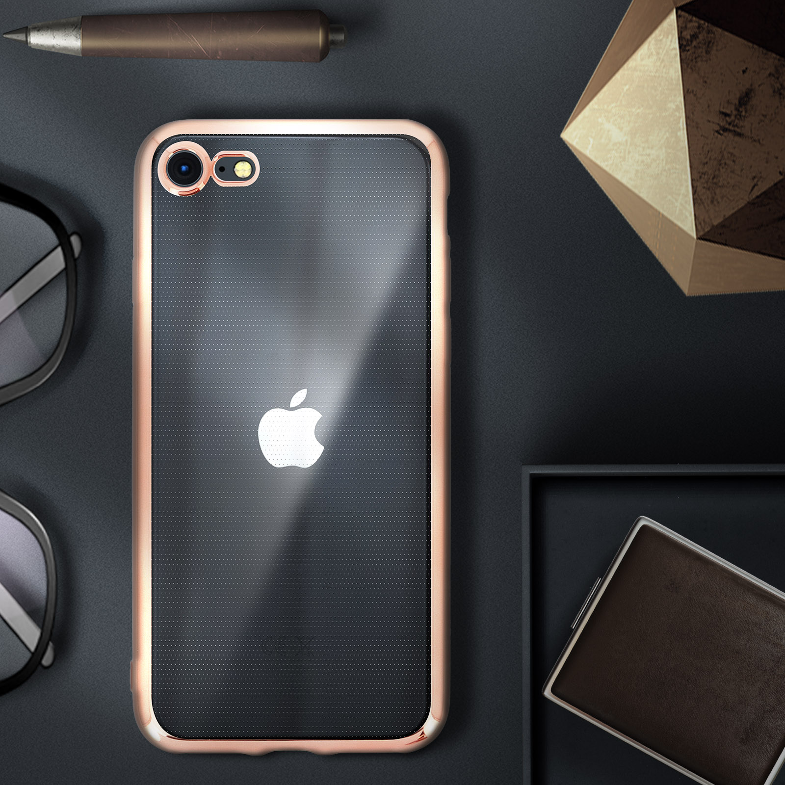 Un telefono in una custodia con il logo Apple, occhiali, una penna, un oggetto geometrico e una piccola scatola.