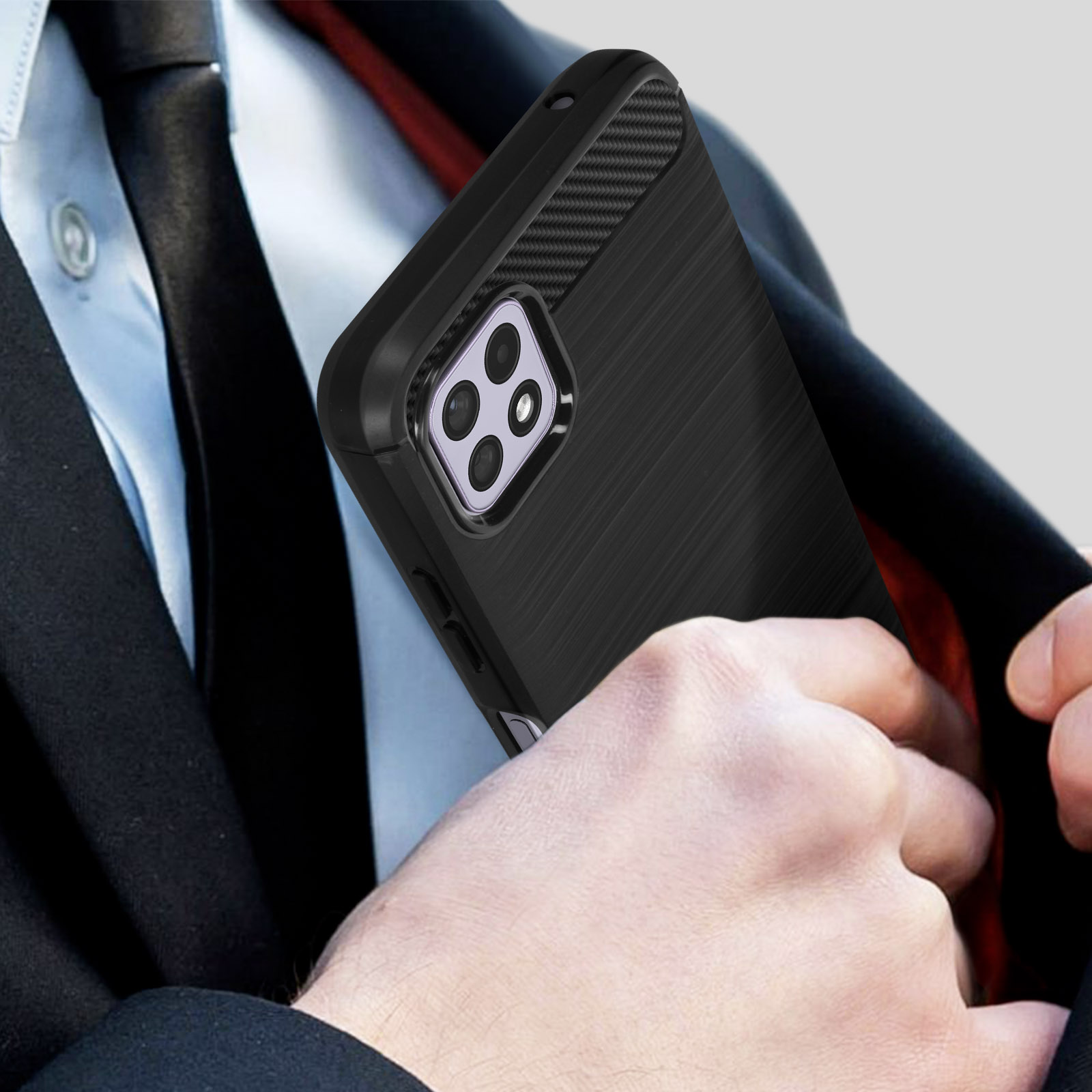 Una mano che mette una custodia nera per telefono con più fotocamere in una tasca della giacca. L'abito è nero, la camicia è bianca.