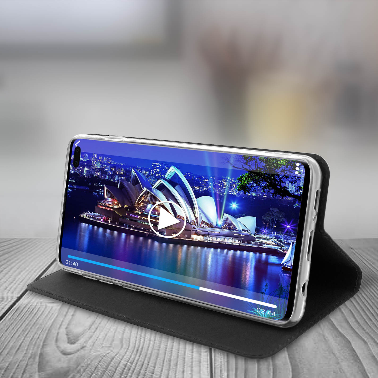 Telefono con video della Sydney Opera House. Custodia nera su tavolo di legno. Pulsante di riproduzione visibile.