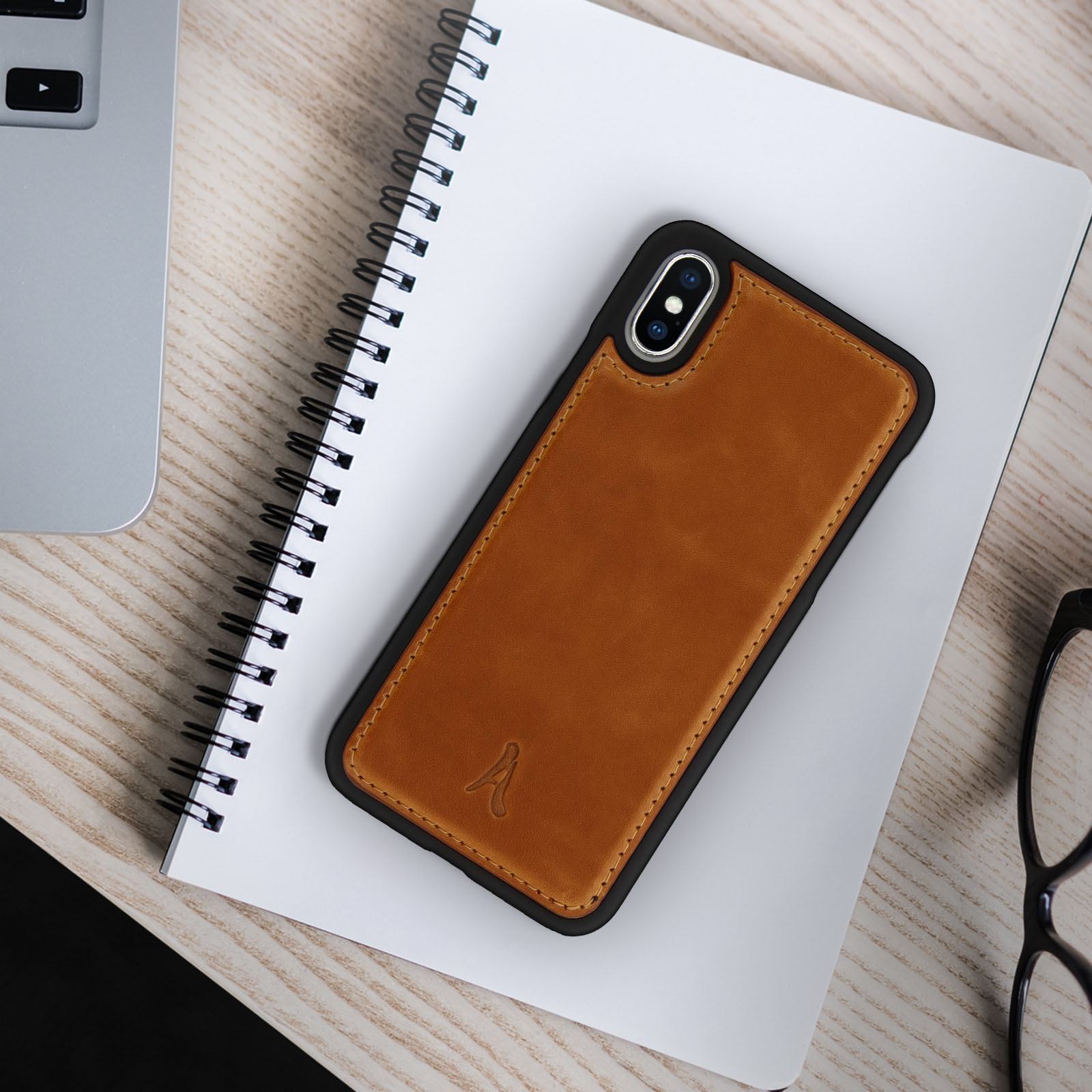Un telefono in una custodia di pelle marrone poggia su un quaderno bianco. La scena è su una superficie di legno.