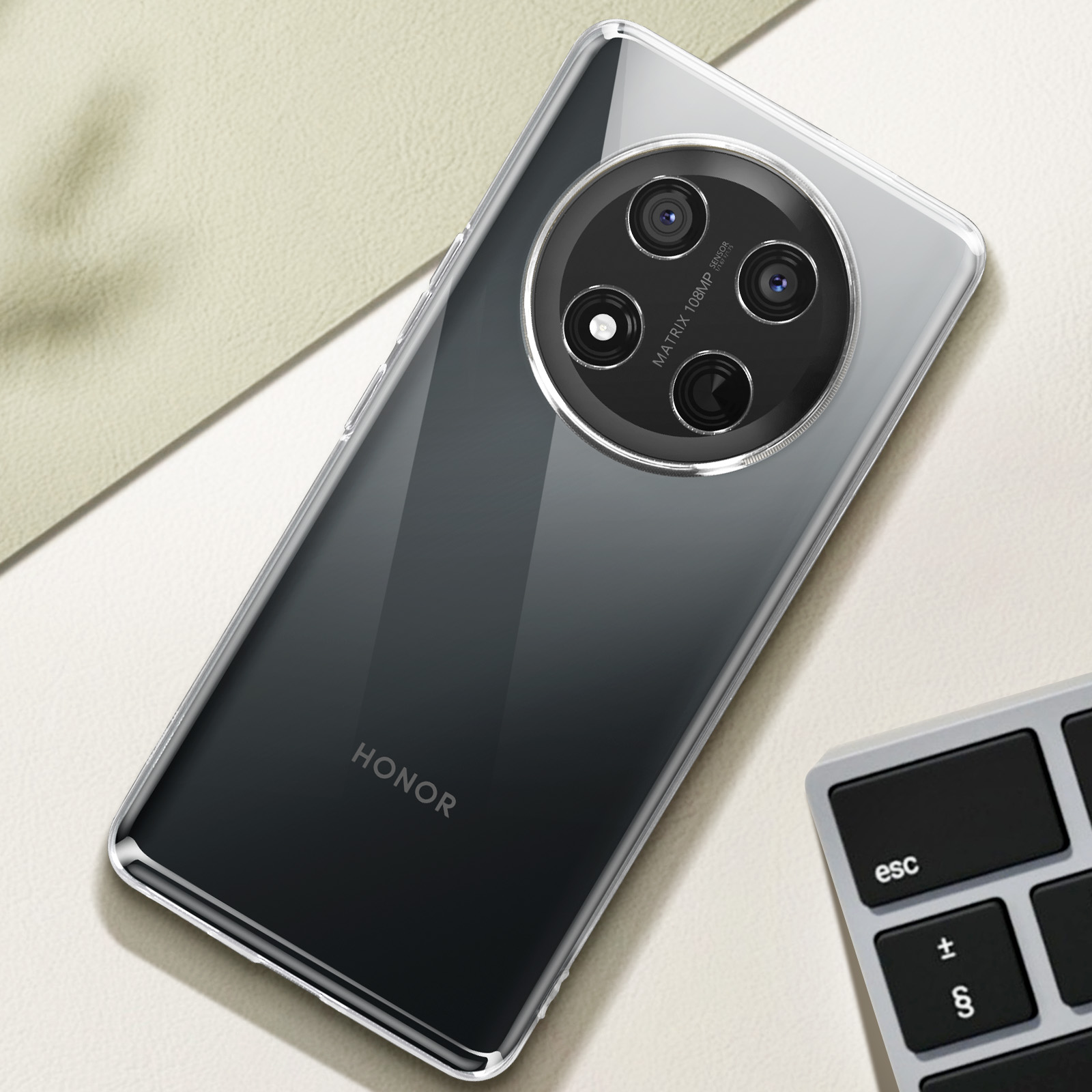 Uno smartphone con custodia trasparente su una superficie beige. Una tastiera sullo sfondo.