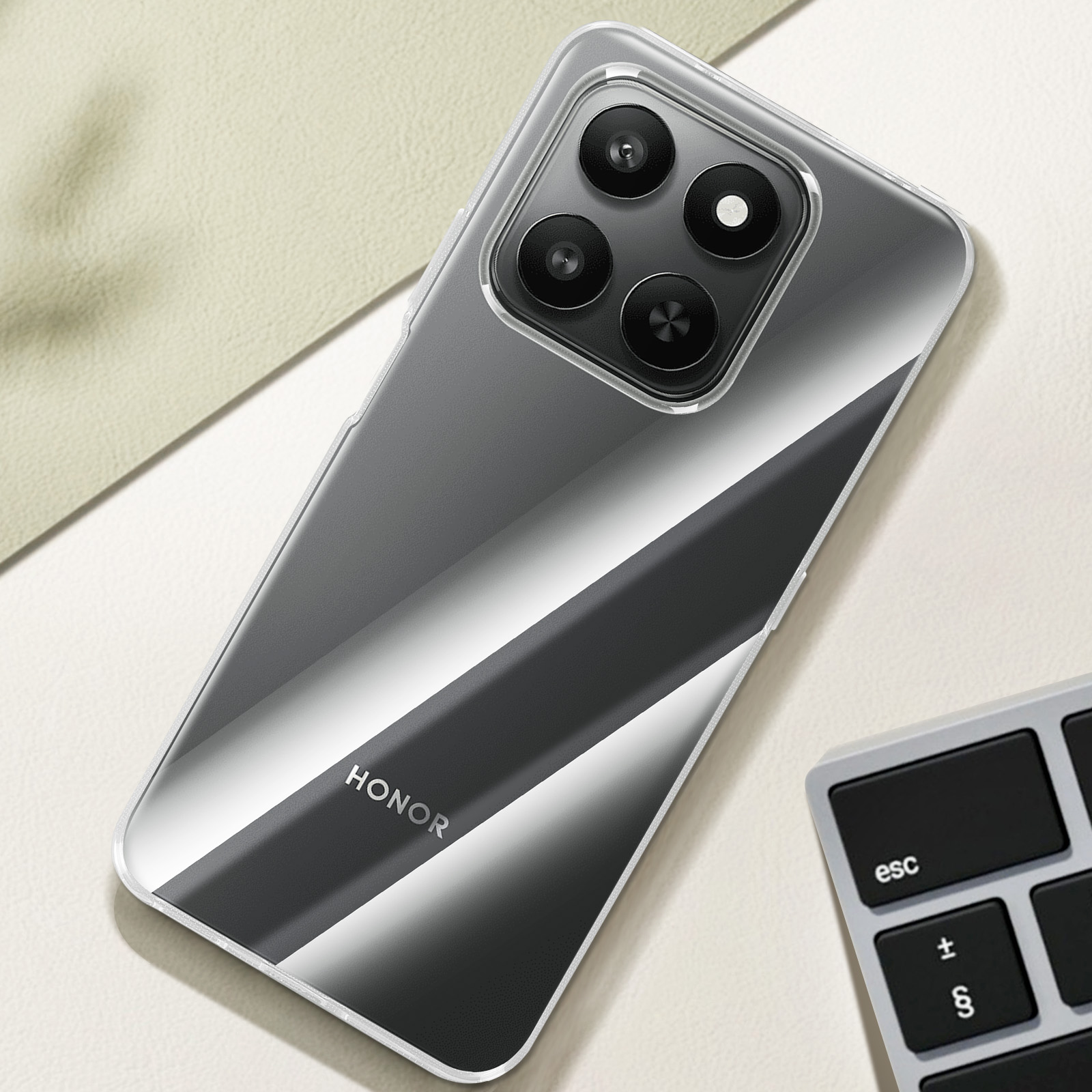 Uno smartphone con custodia trasparente, con quattro obiettivi. Il telefono ha un design sfumato, accanto a una tastiera.