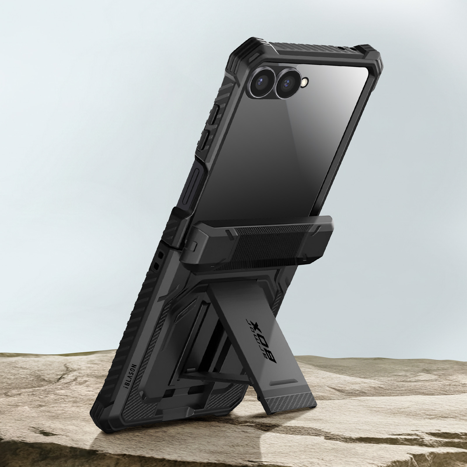 Zwarte telefoon met hoes, ondersteund door een standaard. De hoes heeft een camera en de telefoon staat op zand.