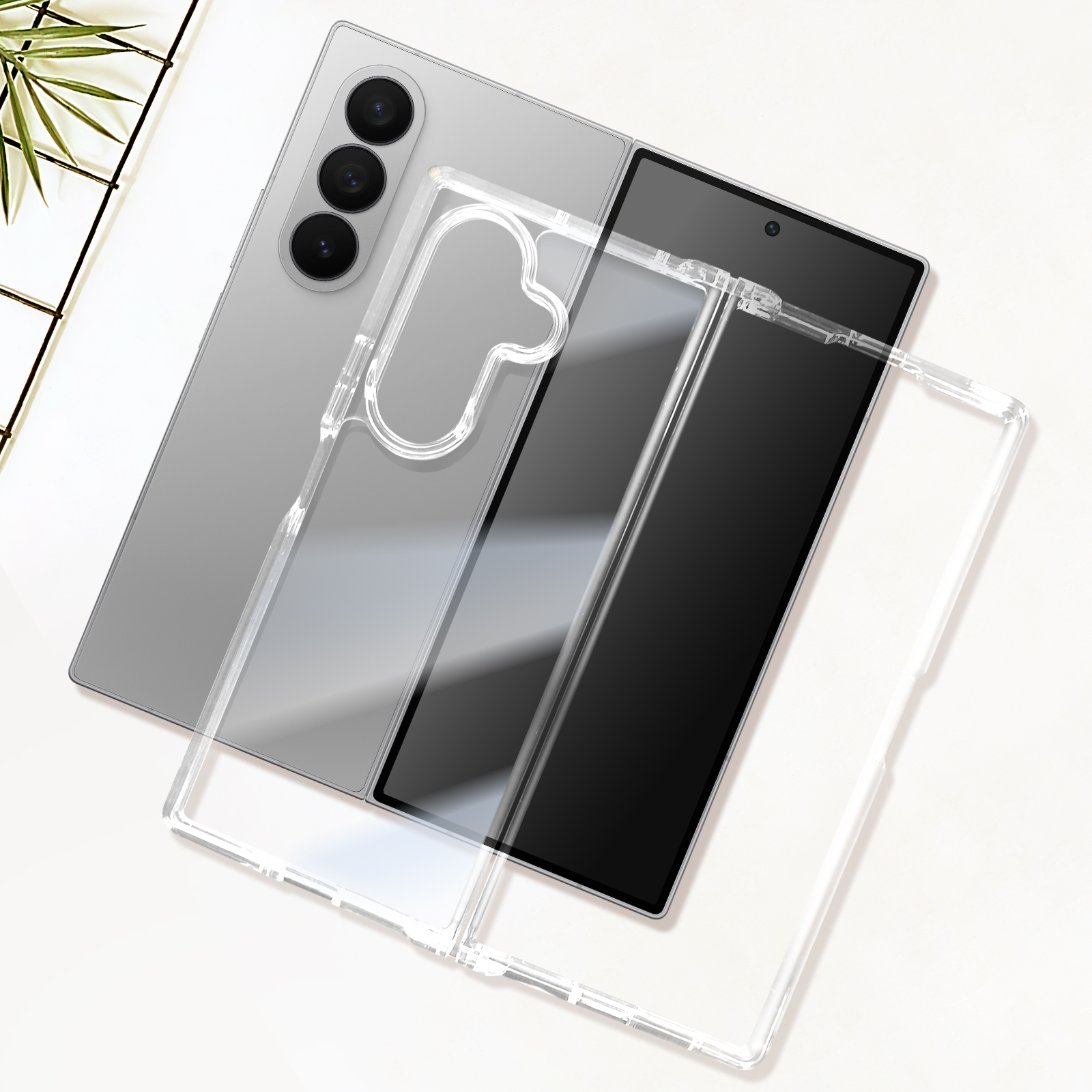 Un smartphone gris plegable con una funda transparente sobre una superficie blanca con una planta.