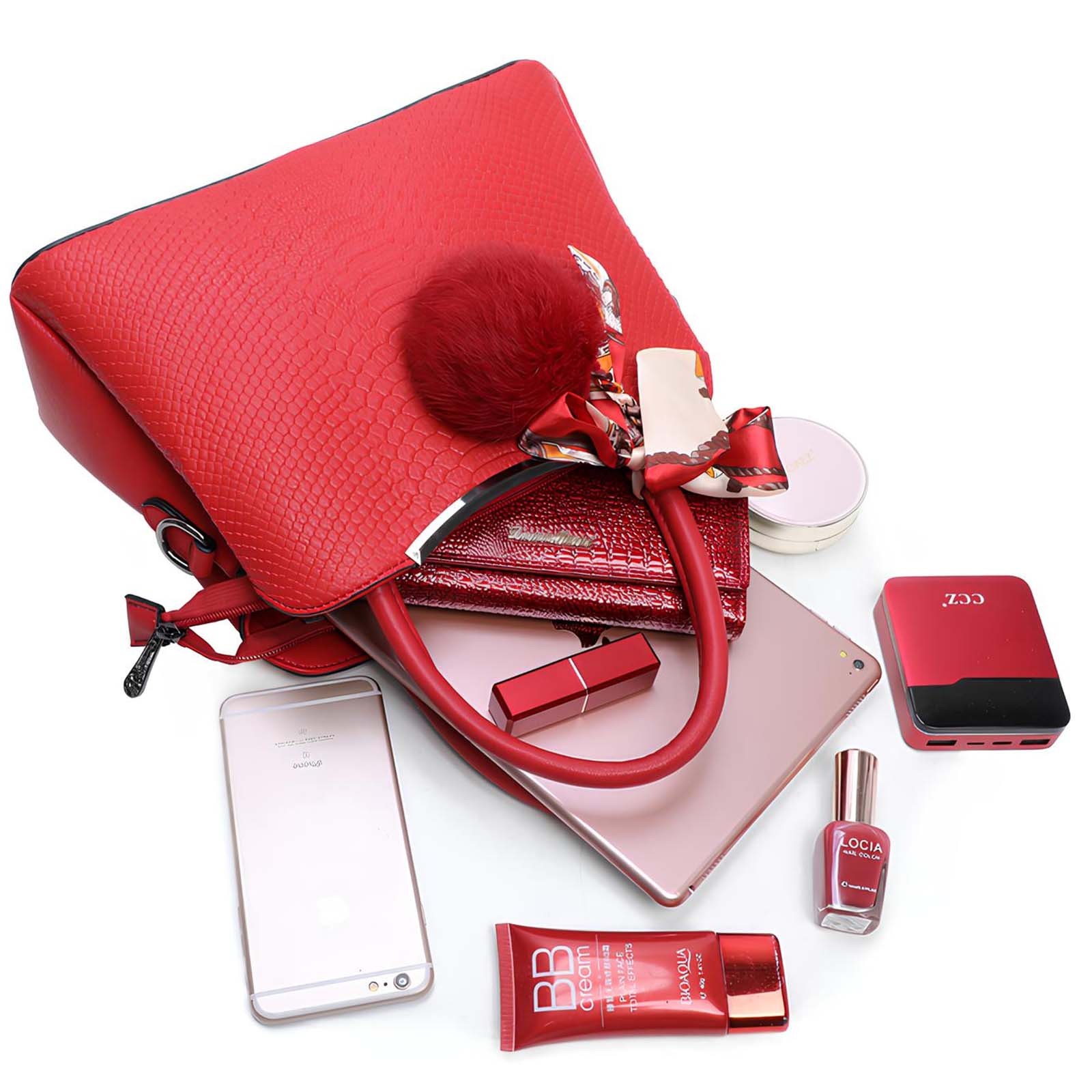 Bolso rojo, teléfono, maquillaje y tableta sobre superficie blanca. Incluye lápiz labial, esmalte y banco de energía.